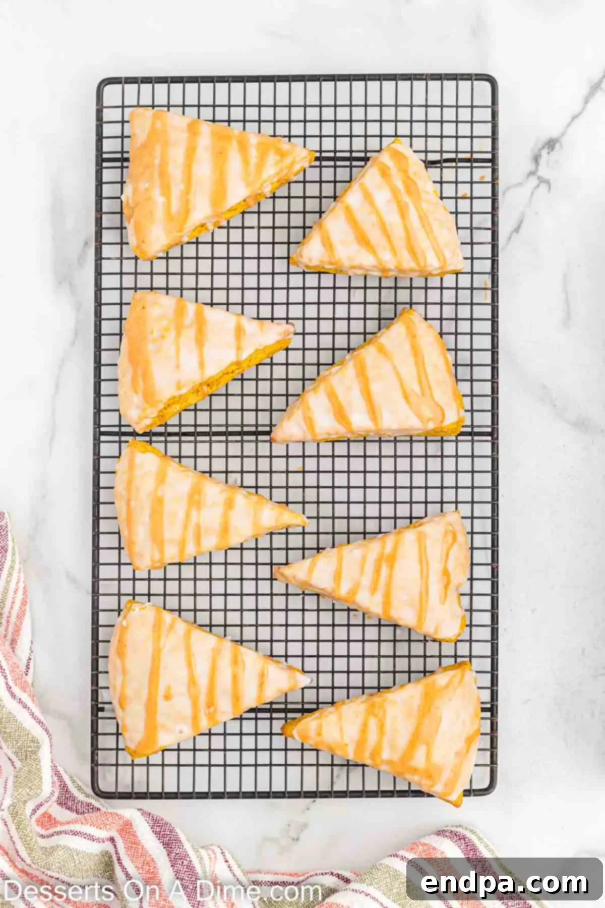 Pumpkin scones on a wire rack, with a layer of white glaze already set and the spiced pumpkin glaze being drizzled on top from a piping bag.