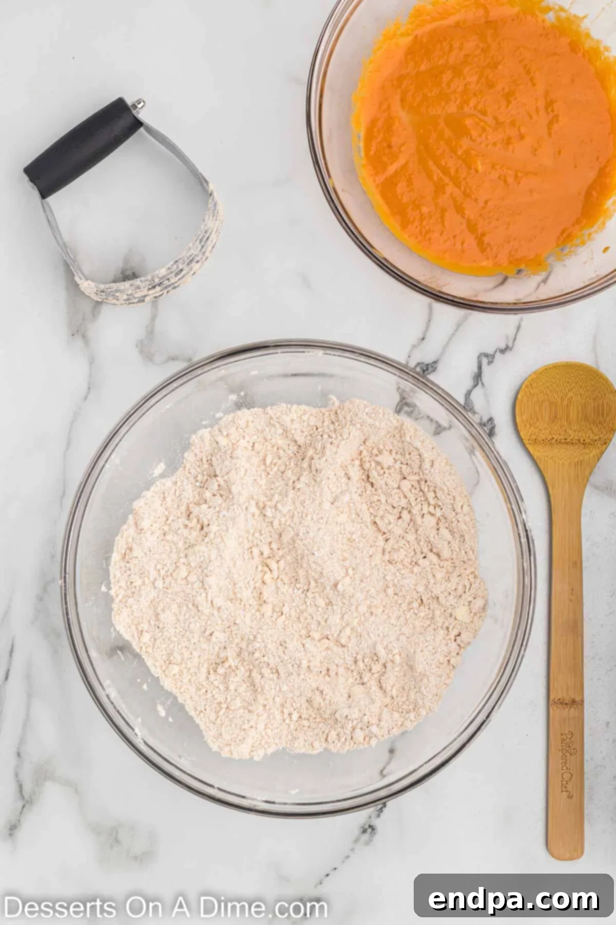 Cold, cubed butter being cut into the dry ingredients for pumpkin scones using a pastry cutter, creating a coarse, crumbly mixture.