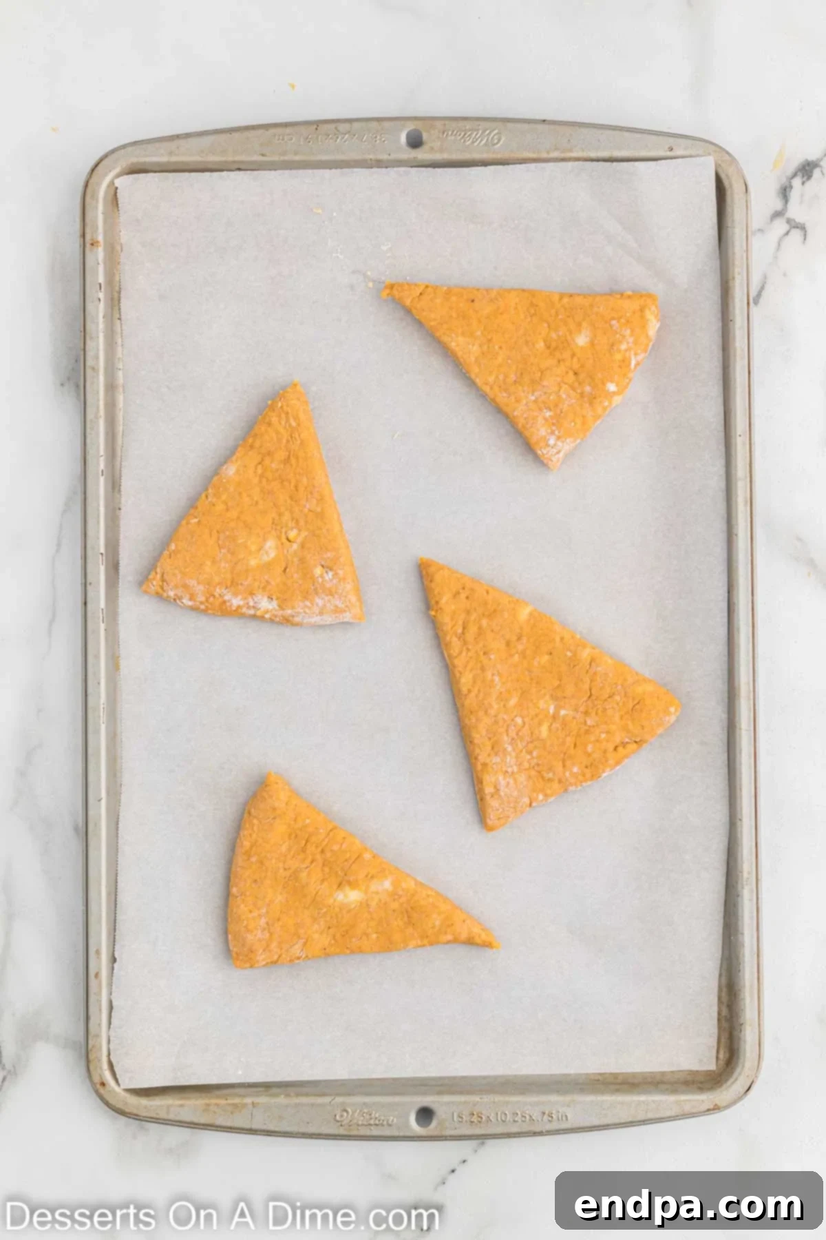 Triangular scone wedges carefully arranged on a parchment-lined baking sheet, ready for the oven.