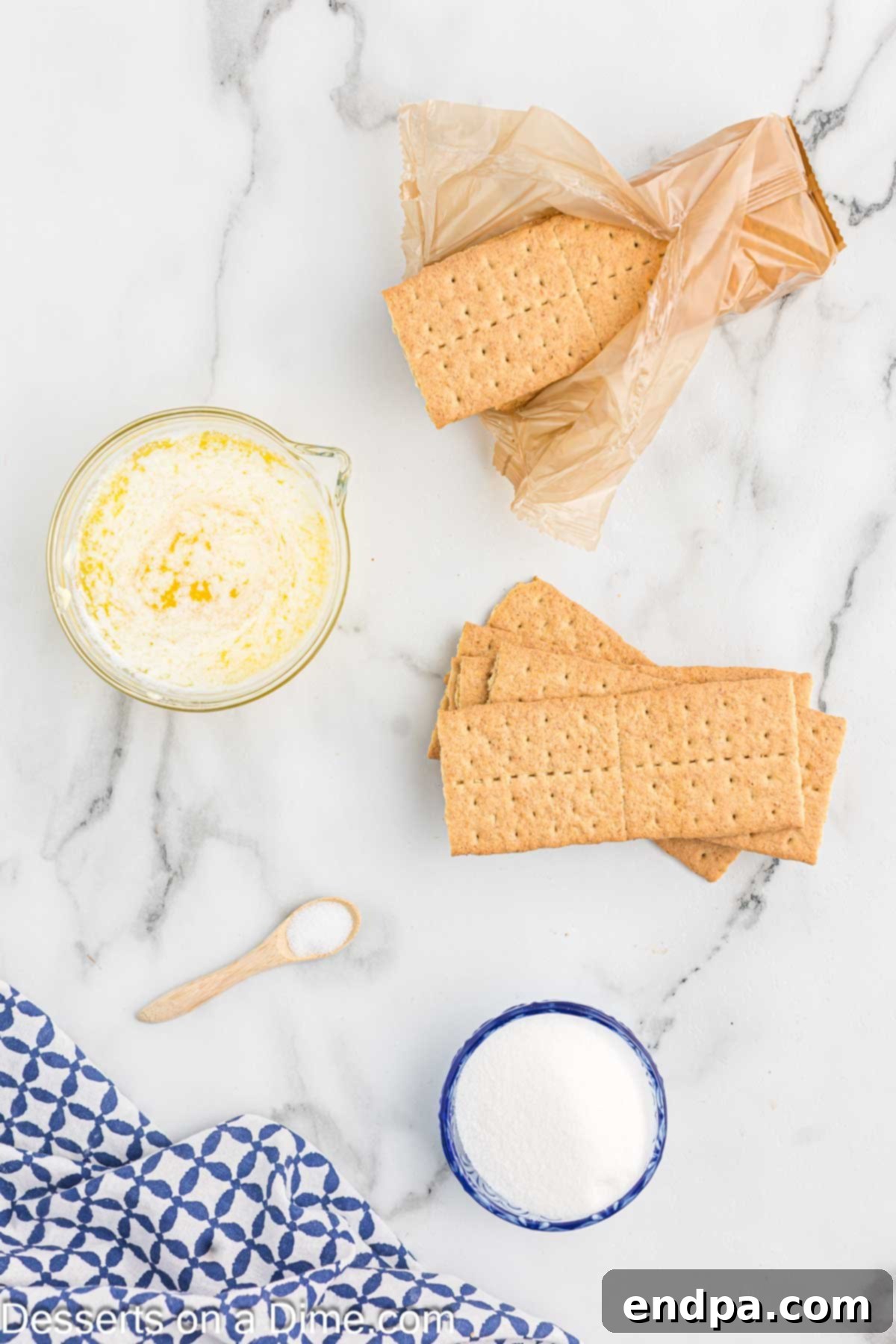 Ingredients laid out for making graham cracker crust: graham cracker crumbs, granulated sugar, salt, and a stick of unsalted butter, clearly visible on a white surface.
