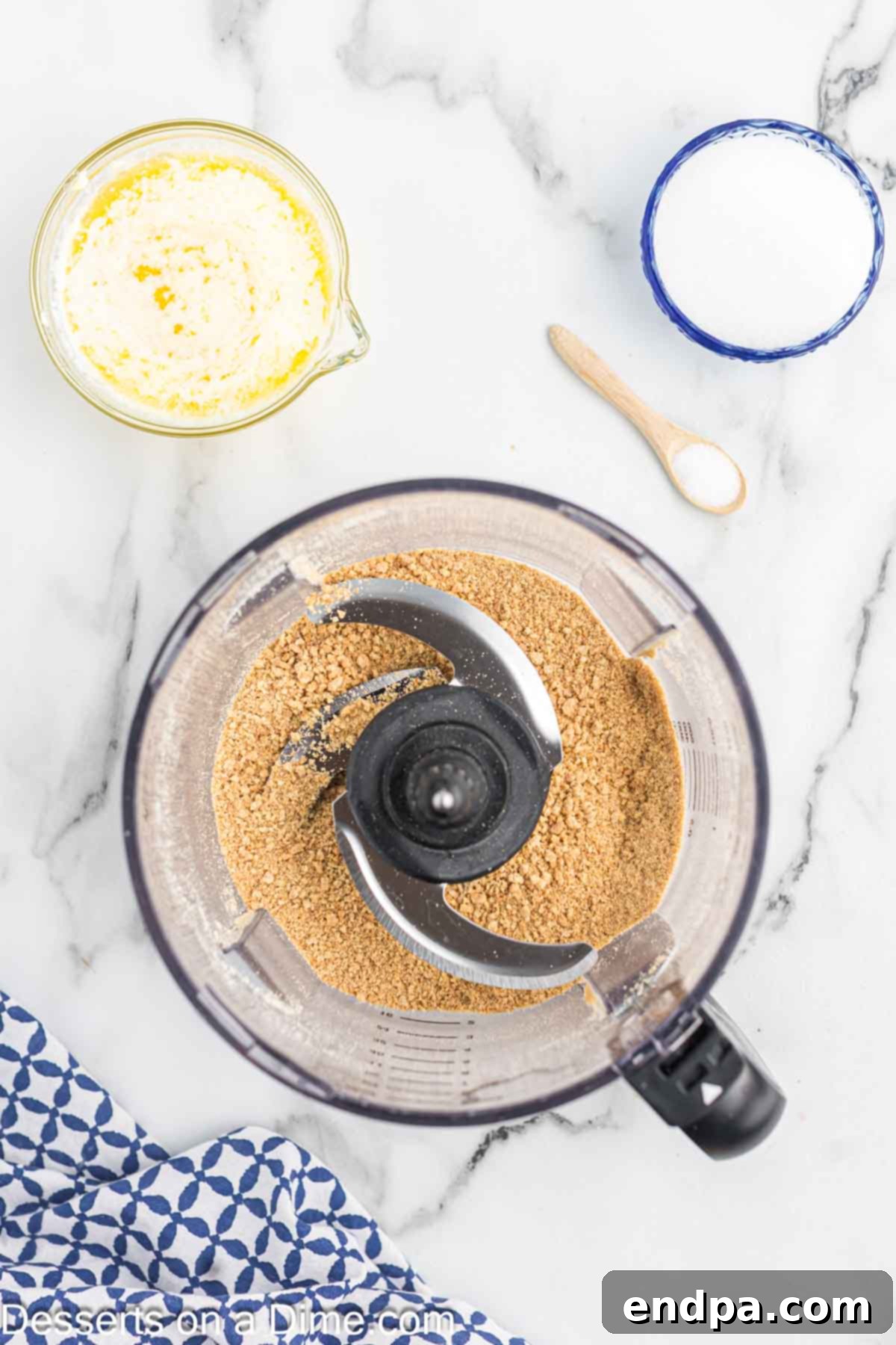Whole graham crackers being crushed into fine crumbs in a food processor, showing the process of turning sheets into powder.