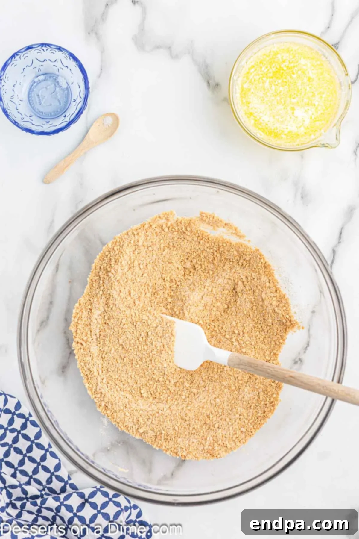 Granulated sugar and salt have been added to the graham cracker crumbs in a bowl, awaiting stirring.