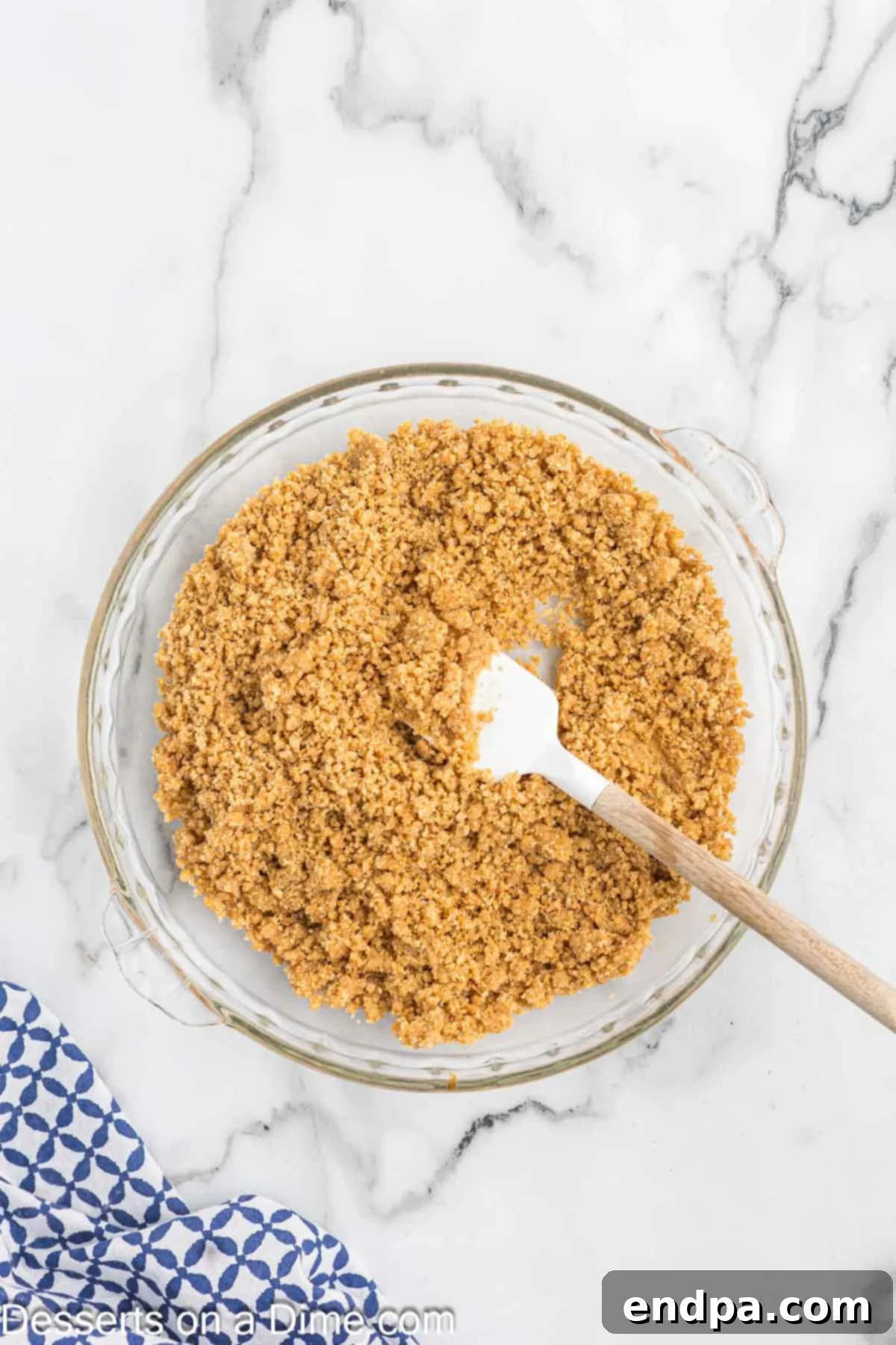 The graham cracker mixture being poured and gently spread into a pie pan, forming an initial layer.