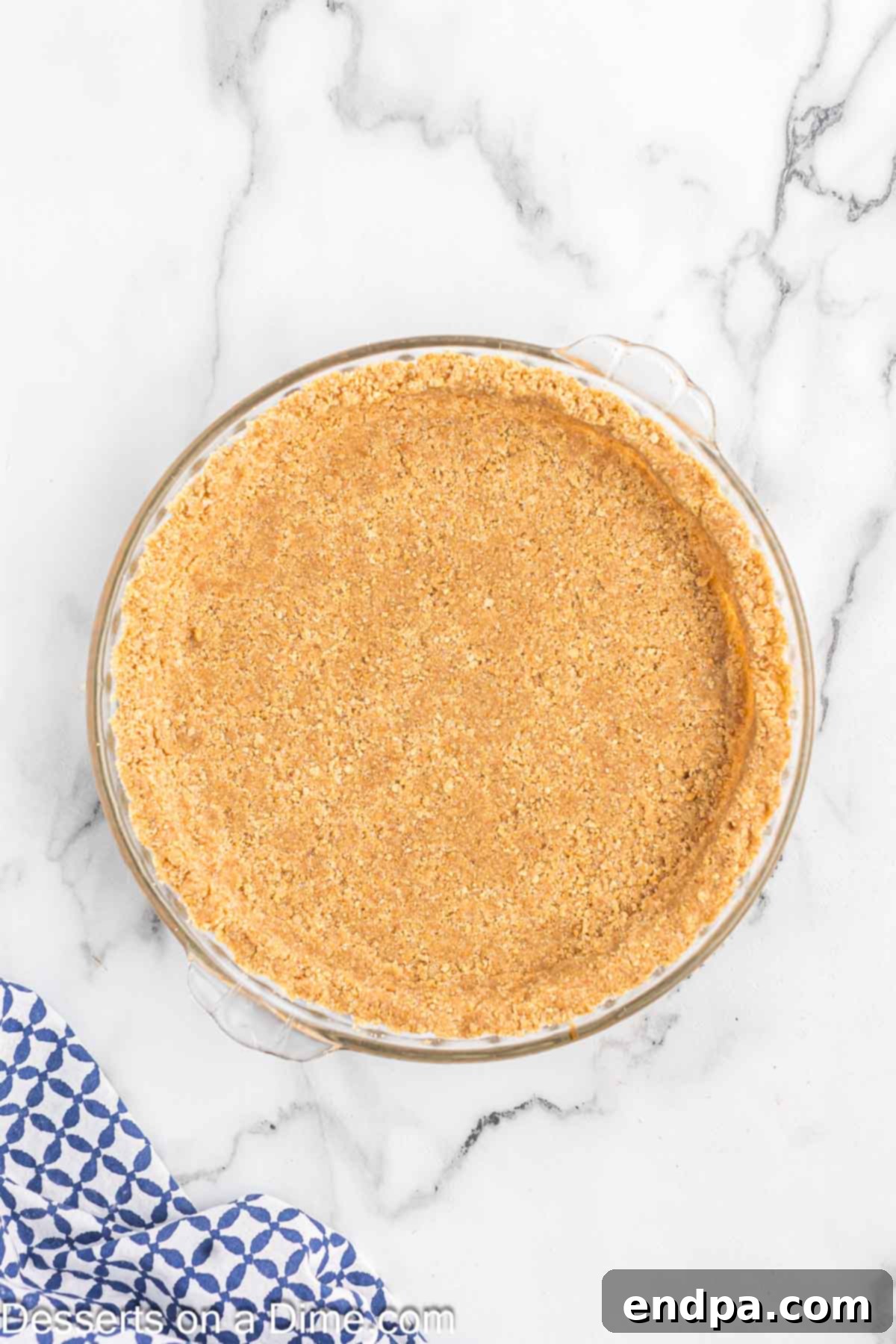 The graham cracker mixture firmly pressed into the bottom and sides of a pie plate using a flat-bottomed glass, demonstrating proper compaction.