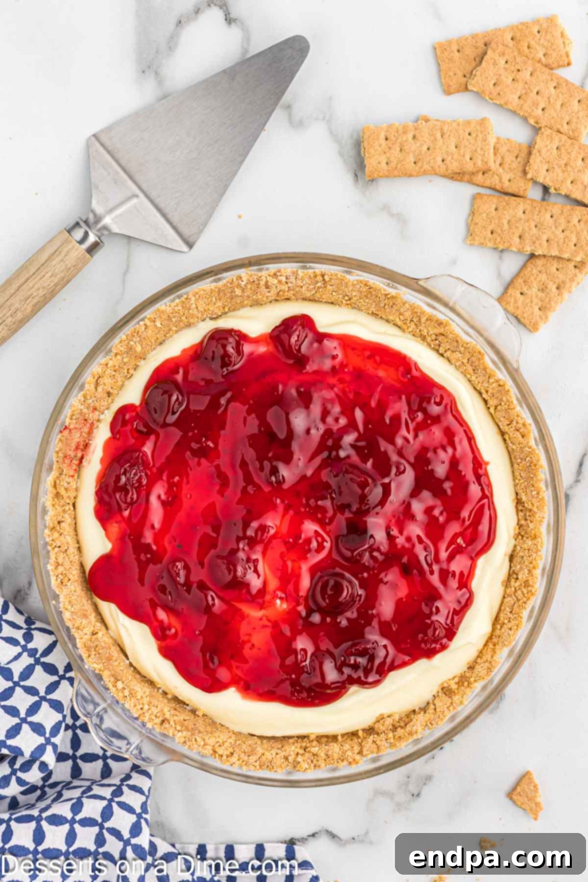 A completed graham cracker crust filled with creamy cheesecake and topped with bright red cherry pie filling, showcasing its versatility and delicious appeal.