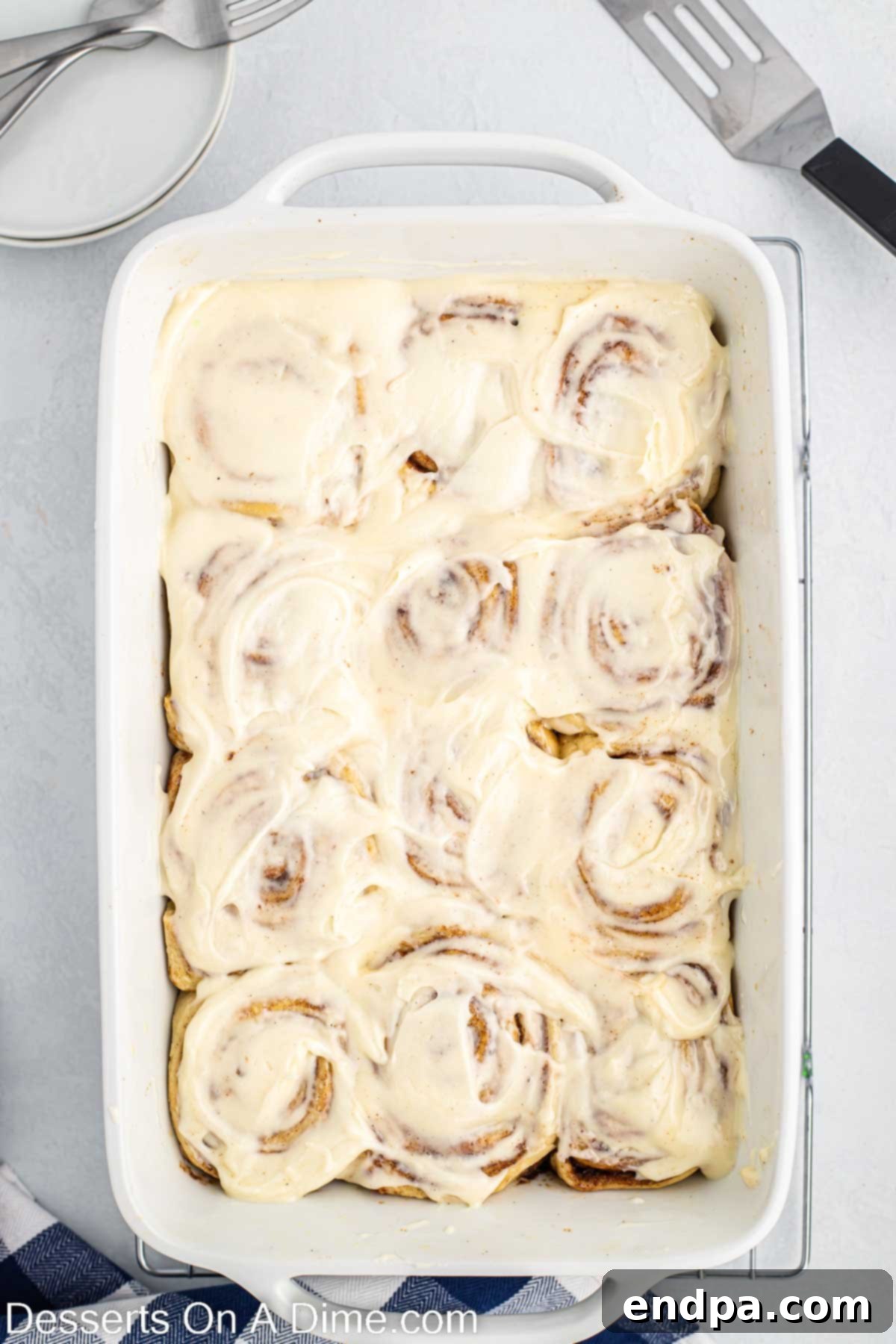 Crafting Perfect Cinnabon Cinnamon Rolls 12 Half of the cream cheese frosting spread over warm, freshly baked Cinnabon Cinnamon Rolls in a baking dish.