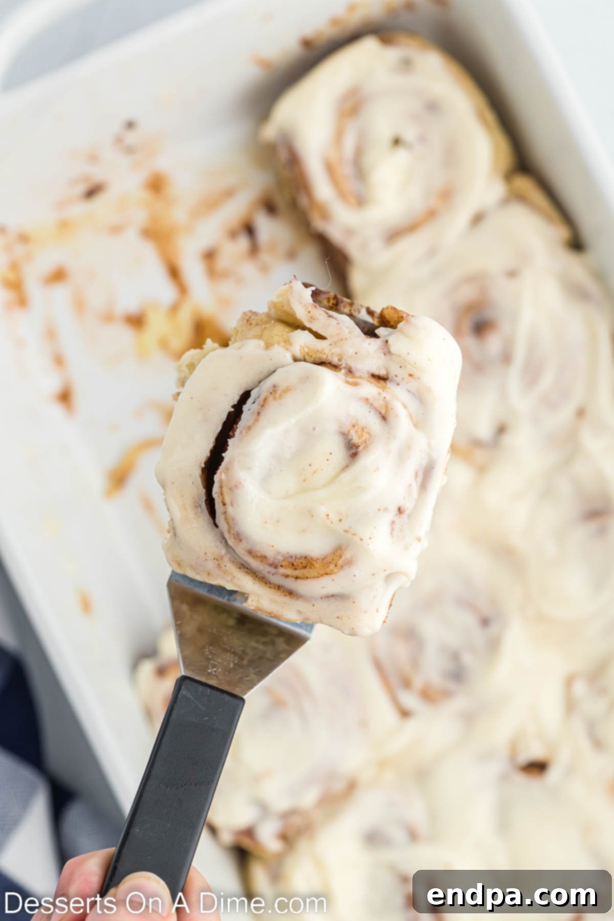 Crafting Perfect Cinnabon Cinnamon Rolls 13 A Cinnabon Cinnamon Roll being served from the baking dish, showcasing its gooey center and thick frosting.