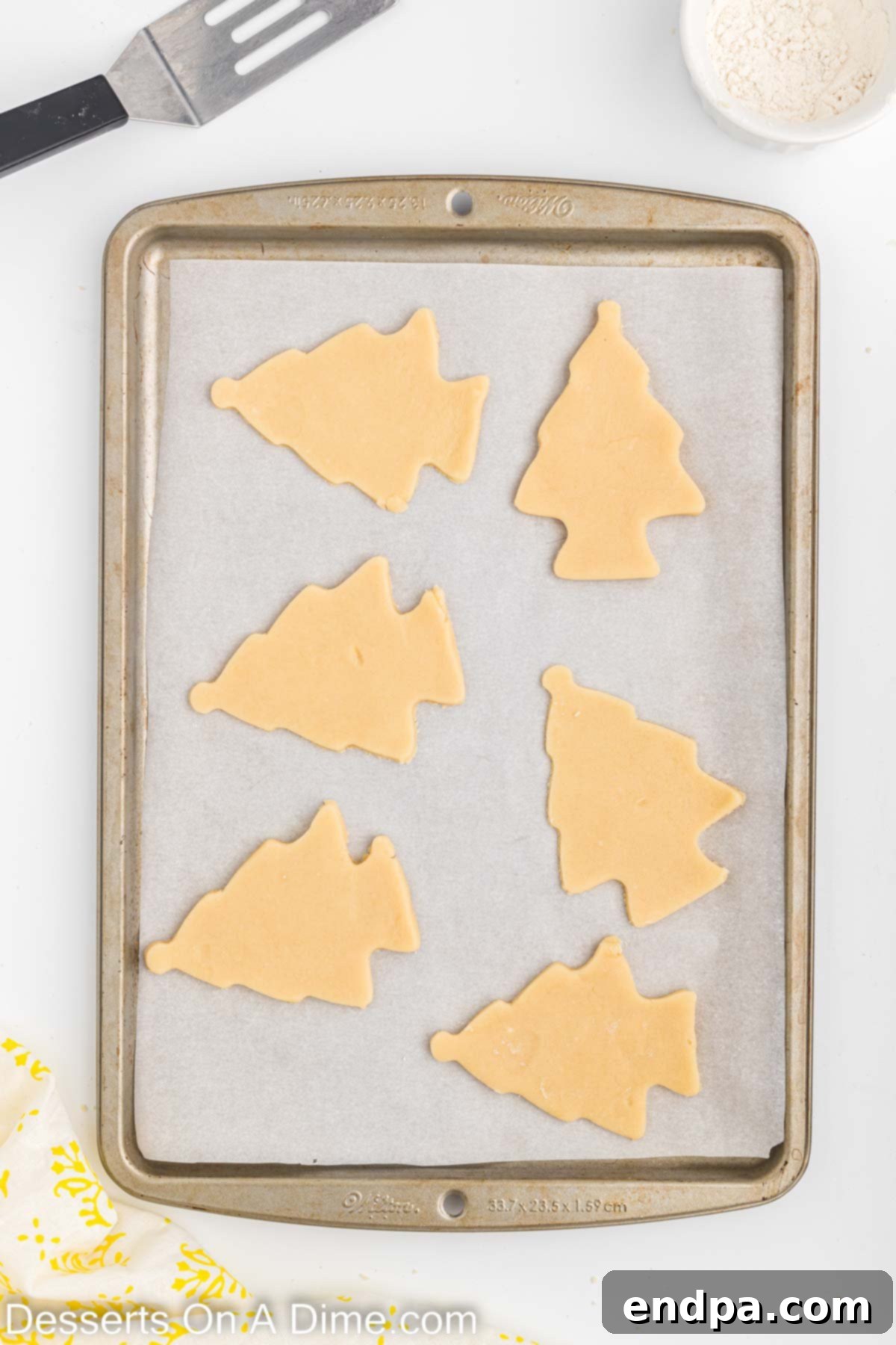 Holiday Tree Sugar Cookie Delights 6 Christmas tree shaped sugar cookie dough cutouts neatly arranged on a parchment-lined baking sheet, ready for the oven.