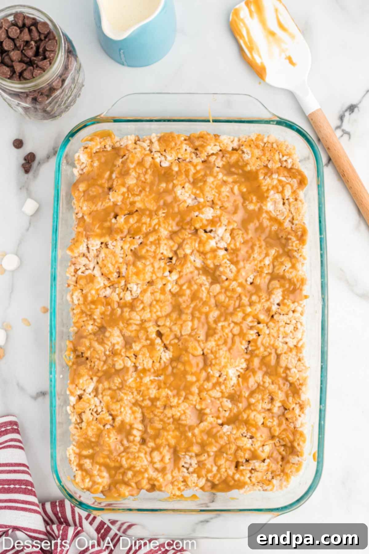 Salted caramel sauce being spread evenly over the chilled Rice Krispie treat base.
