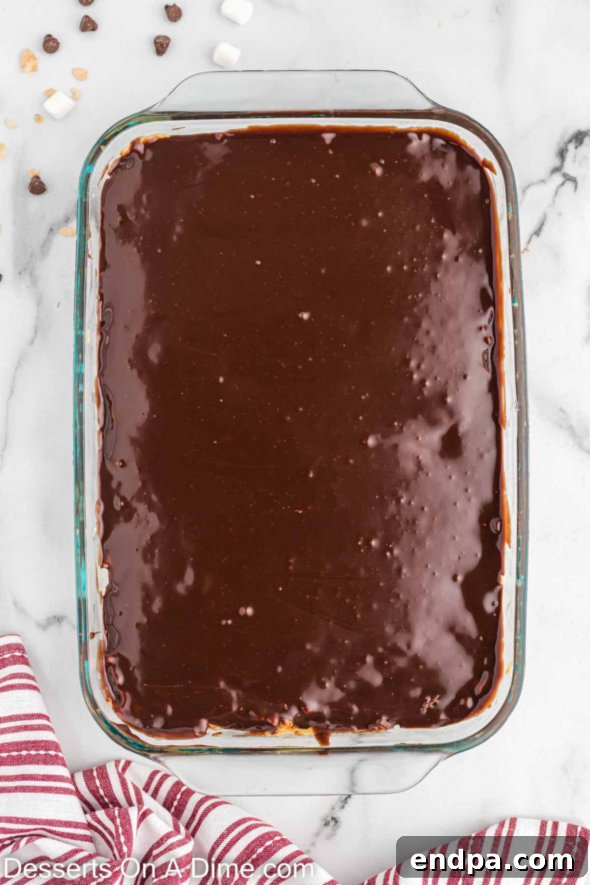 Smooth chocolate ganache being spread over the caramel layer on the Rice Krispie treats.