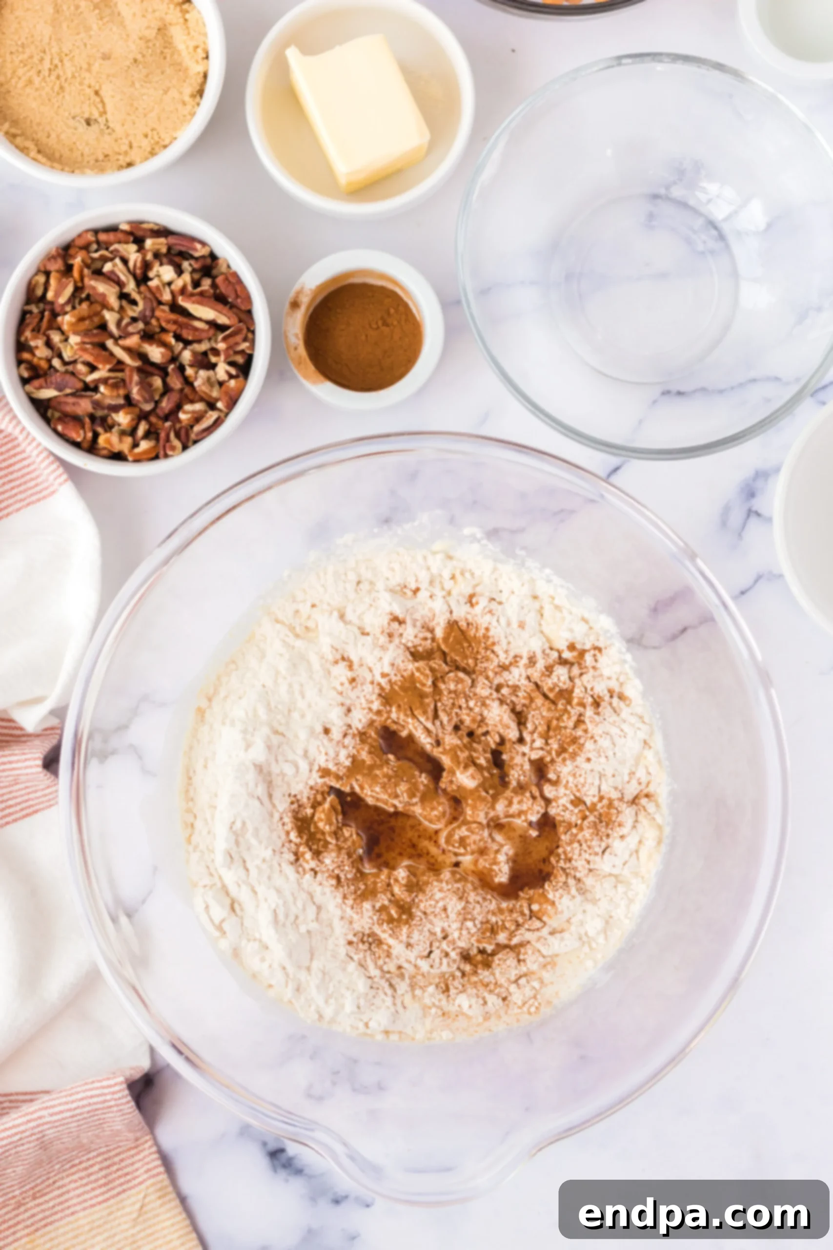 Canola oil, all-purpose flour, and ground cinnamon being added to the activated yeast and milk mixture in a bowl.
