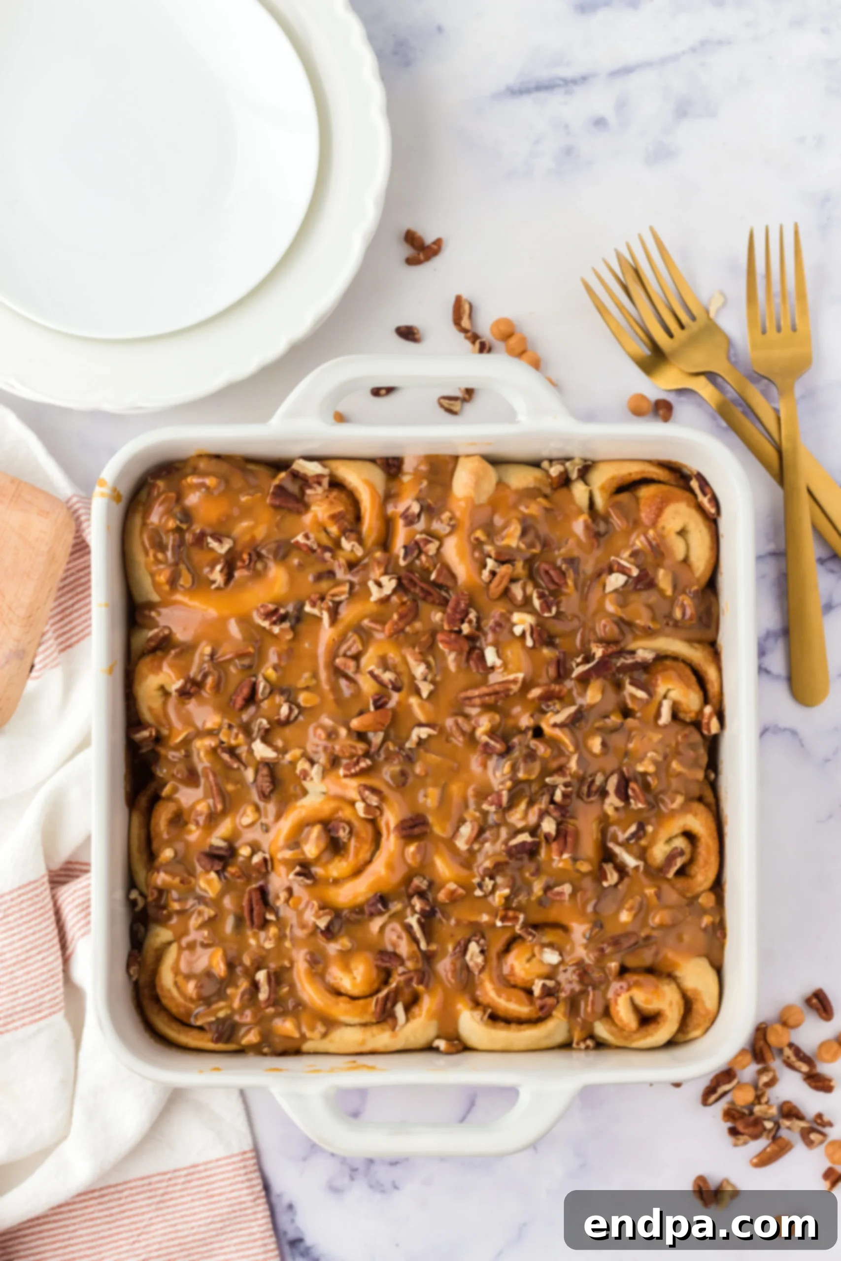 Gooey caramel sauce with chopped pecans being spooned over freshly baked cinnamon rolls.