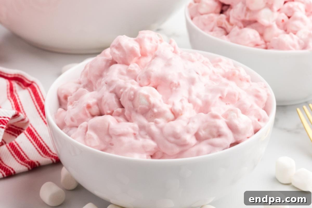 A serving of Cherry Fluff in a bowl, with a spoon digging in to show its fluffy texture.