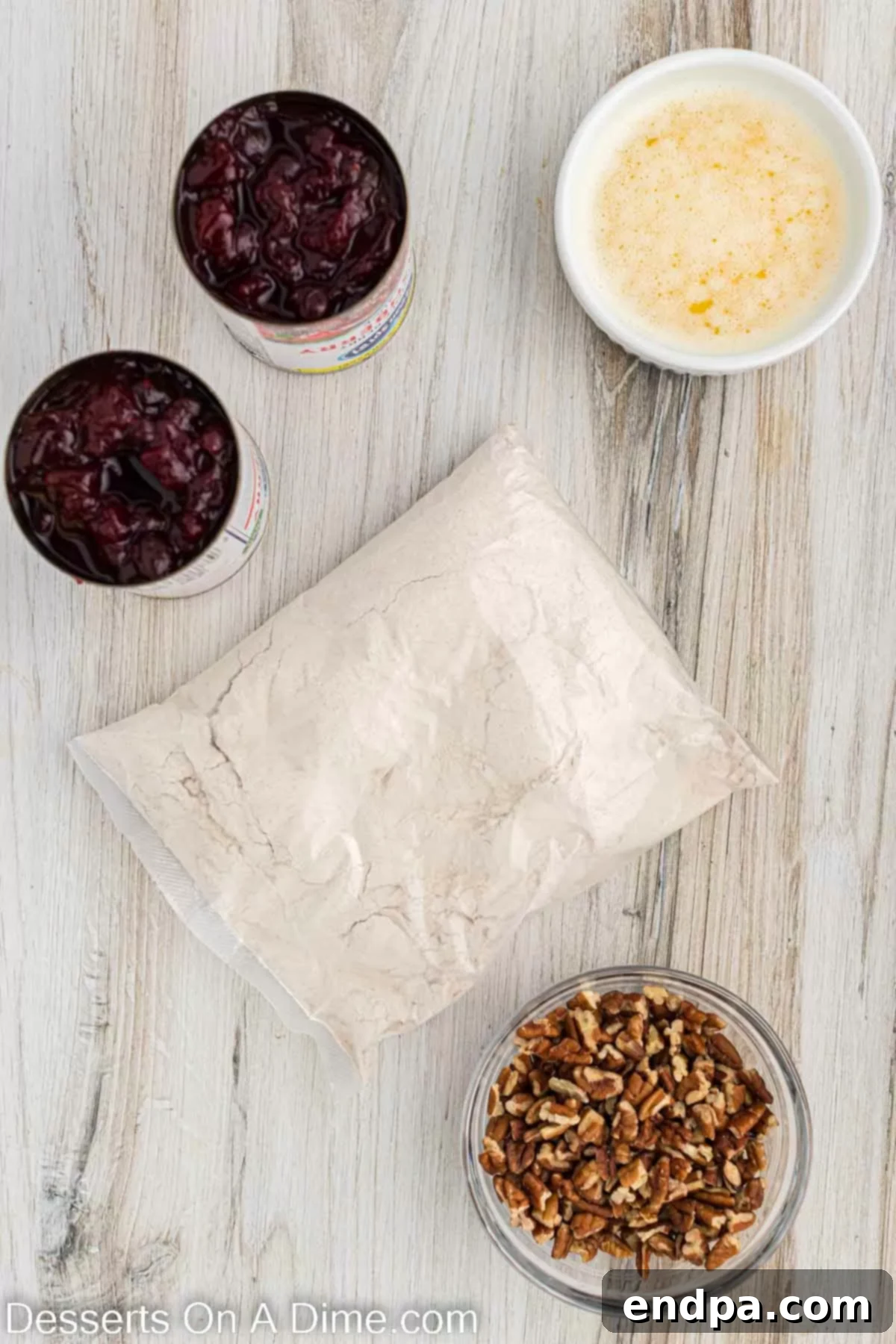 Ingredients laid out for Christmas dump cake: a box of spice cake mix, cans of cranberry sauce, chopped pecans, and sticks of butter.