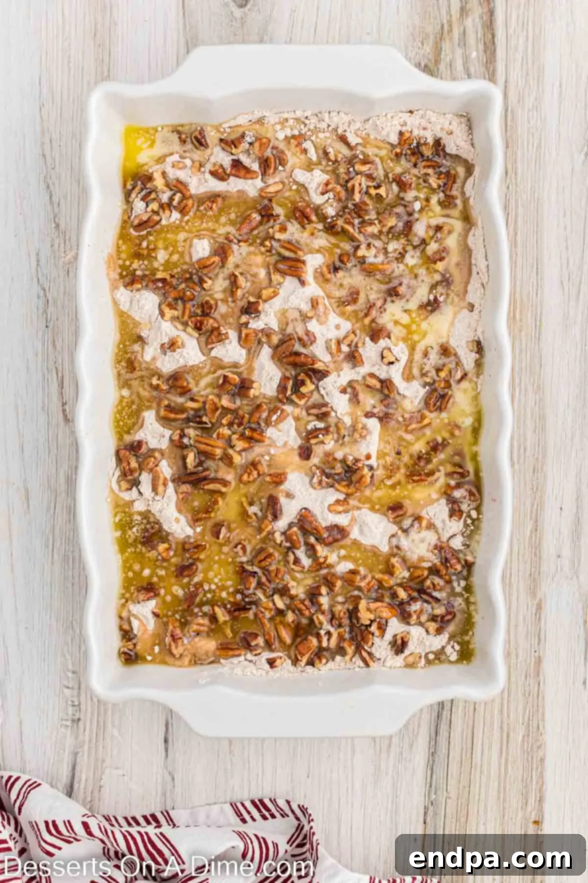 Melted butter being slowly drizzled over the top of the cake mix and pecans.