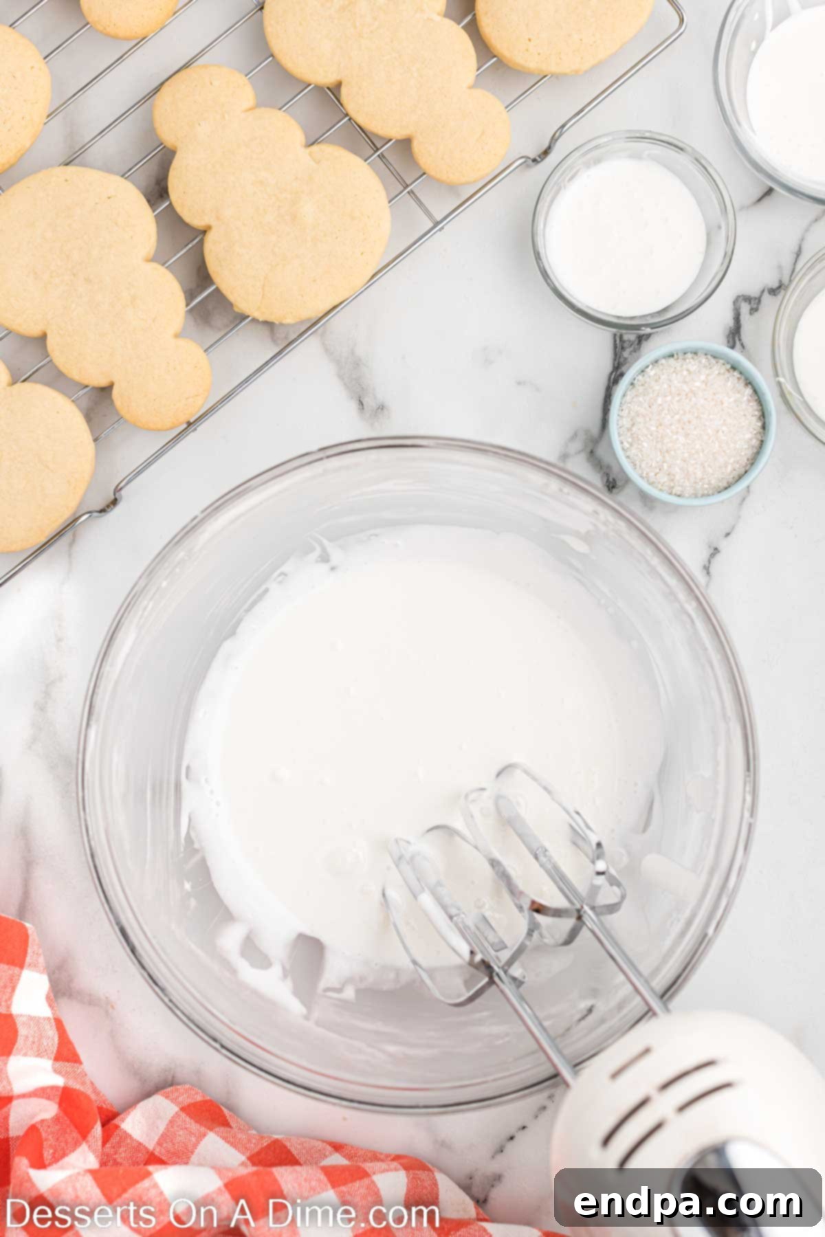 Ingredients for royal icing, including egg whites and powdered sugar, being mixed in a bowl with a hand mixer.