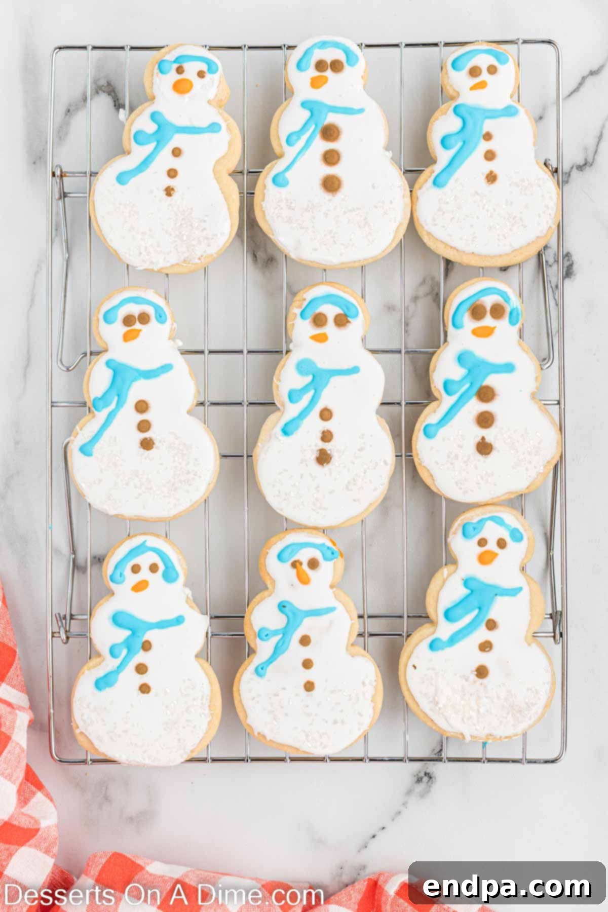 Decorated snowman cookies with faces, buttons, earmuffs, and scarves on a wire rack.