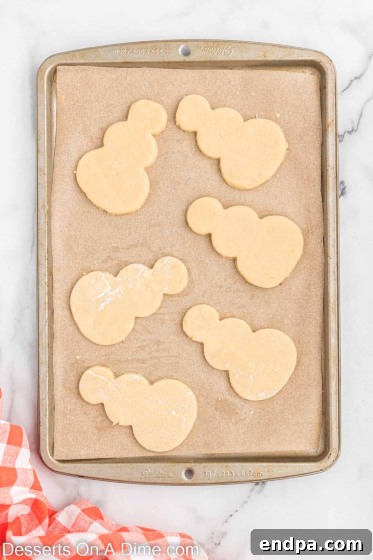 Snowman shaped cookies arranged on a baking sheet lined with parchment paper, ready for baking.
