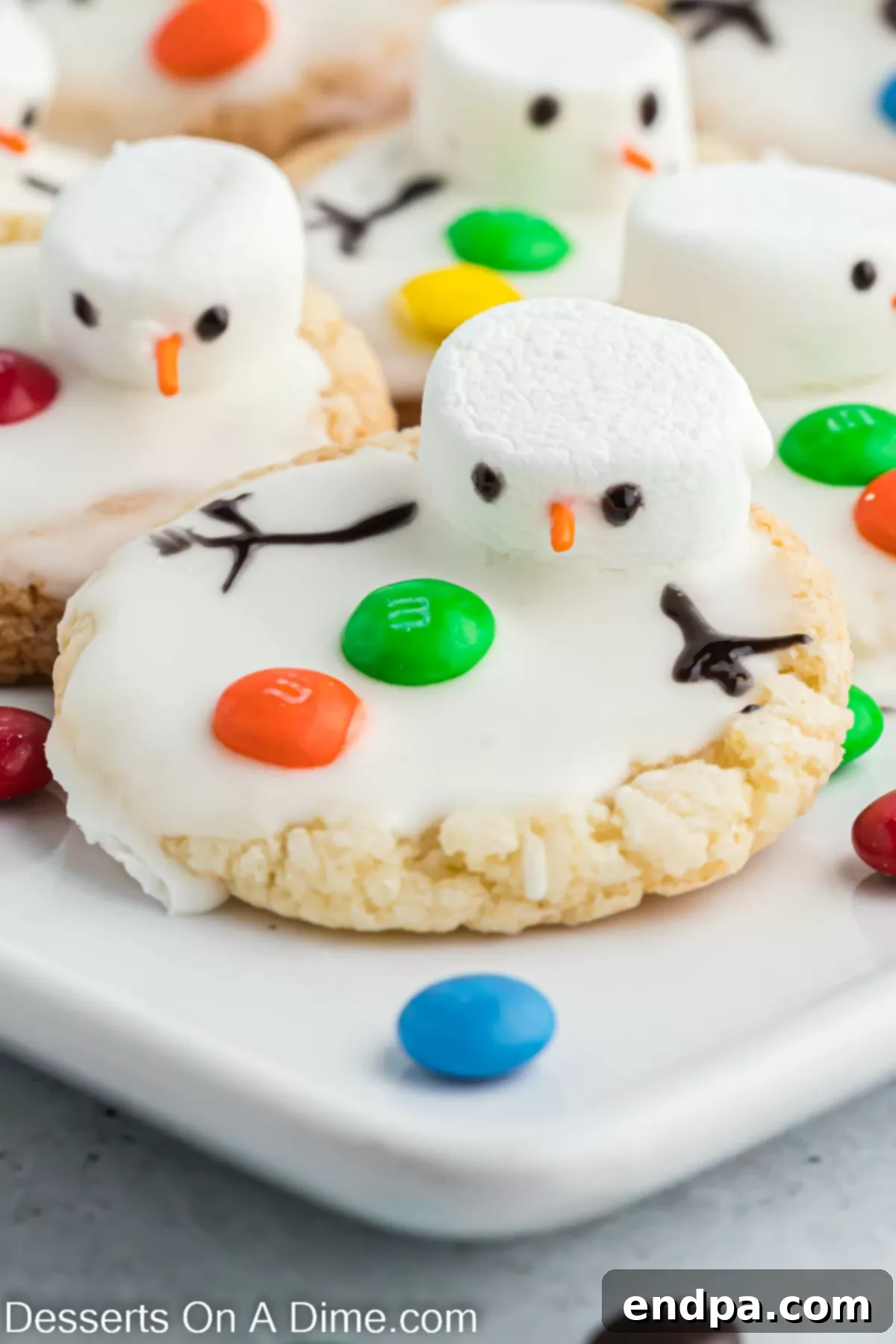Whimsical Melted Snowman Treats 2 Melted snowman cookies up close. These whimsical winter treats feature soft sugar cookies topped with drippy white royal icing, half-marshmallows, candy buttons, and hand-drawn faces, creating the illusion of adorable snowmen that have gently melted.