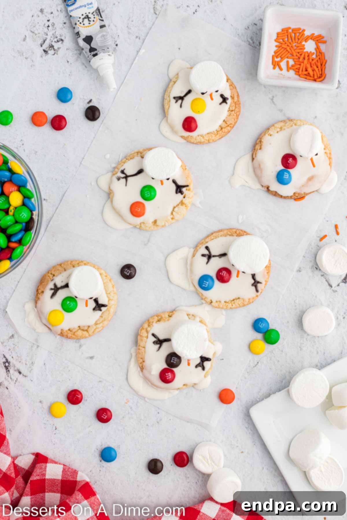 Whimsical Melted Snowman Treats 7 Black icing used to decorate and add arms. A melted snowman cookie is being finished with black decorating gel to pipe the eyes, mouth, and stick arms, bringing the character to life.
