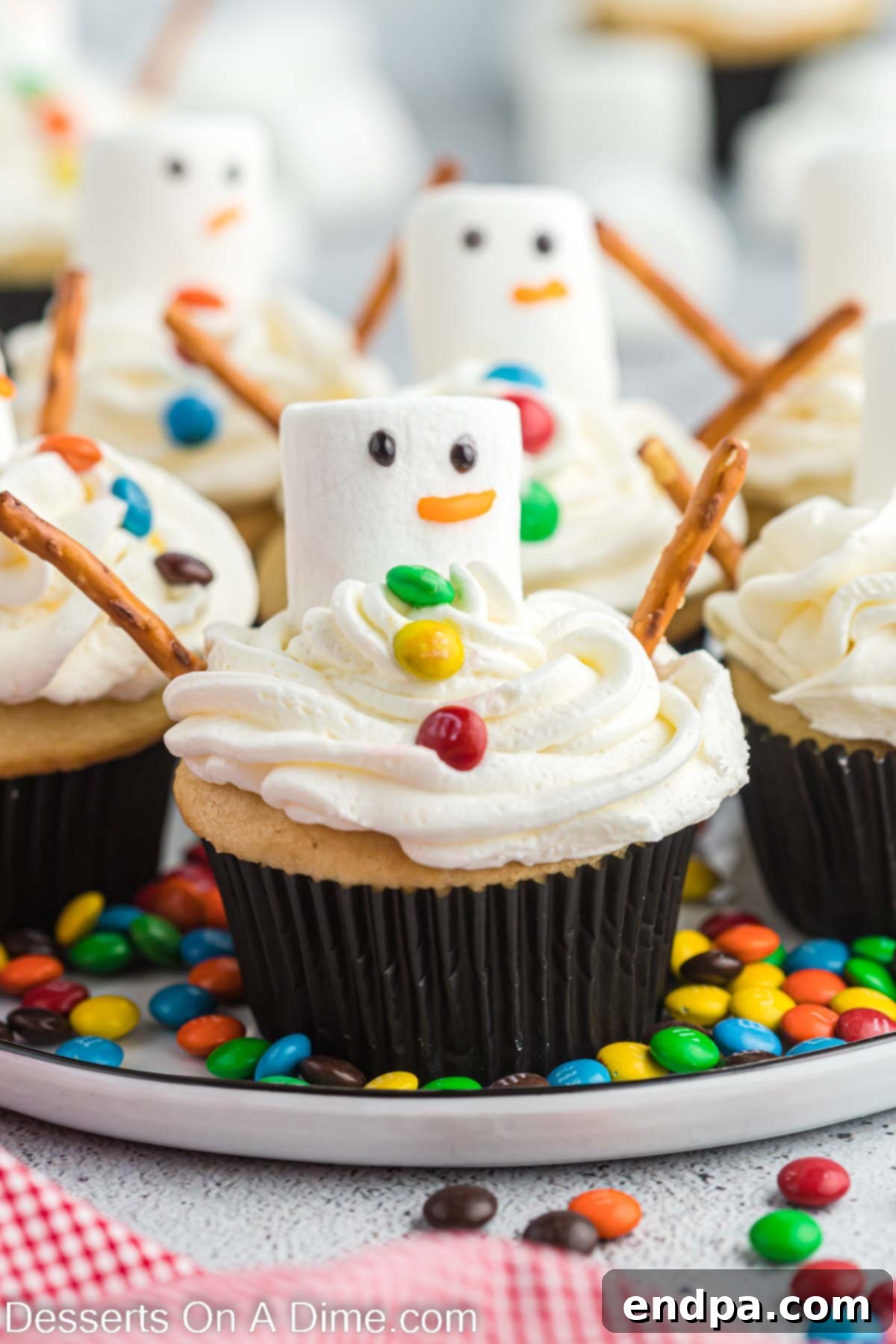 Close-up of adorable melted snowman cupcakes on a festive platter, showcasing their marshmallow heads, candy buttons, and pretzel arms.