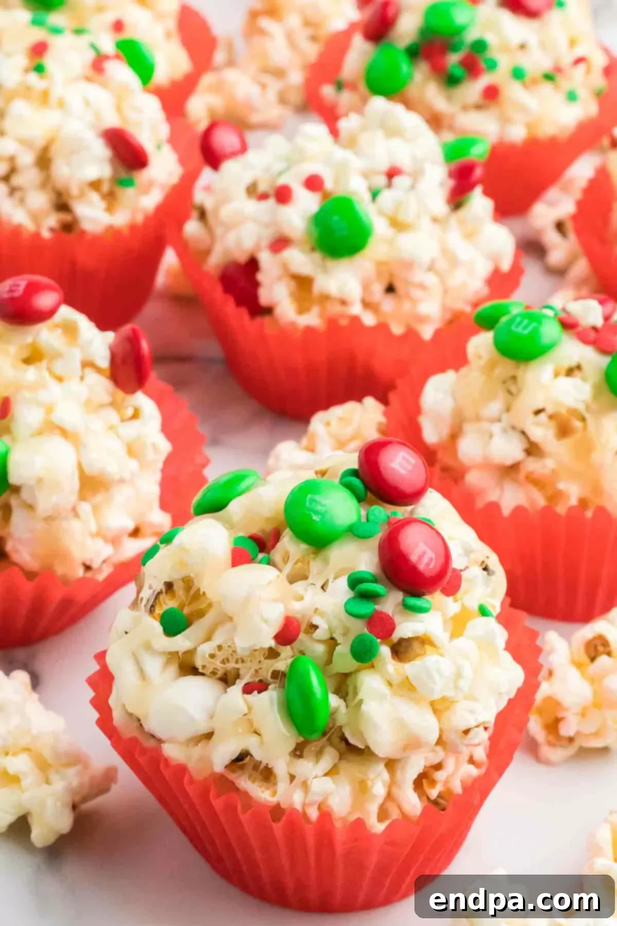 Holiday Popcorn Ball Delight 2 Vibrant Christmas popcorn balls, presented beautifully in red paper muffin liners and adorned with an assortment of festive red, green, and white sprinkles.