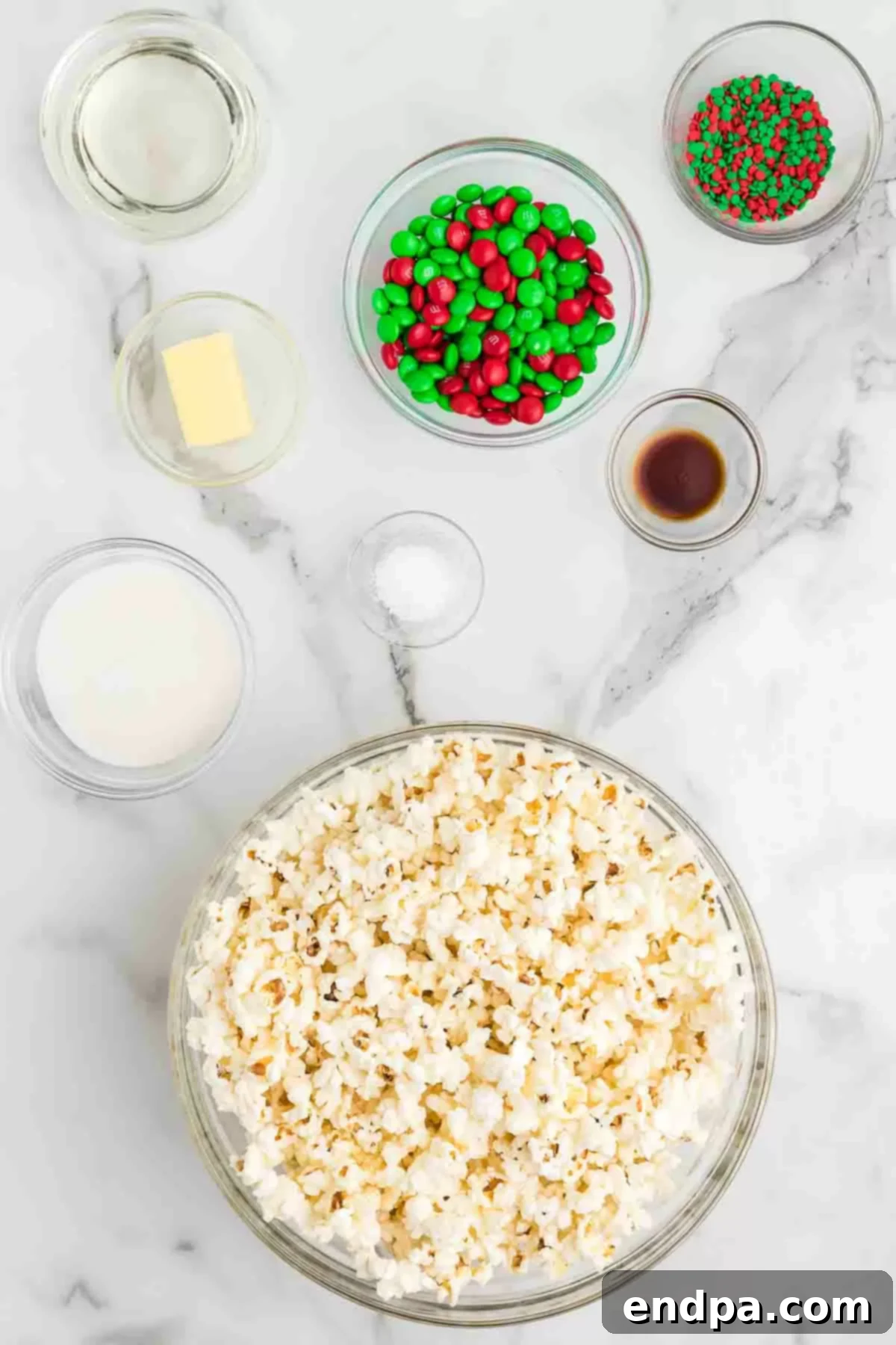 Holiday Popcorn Ball Delight 3 A flat lay photograph displaying the core ingredients required for making Christmas popcorn balls: a bowl of freshly popped popcorn, granulated sugar, a bottle of light corn syrup, a stick of butter, and a container of festive Christmas sprinkles.