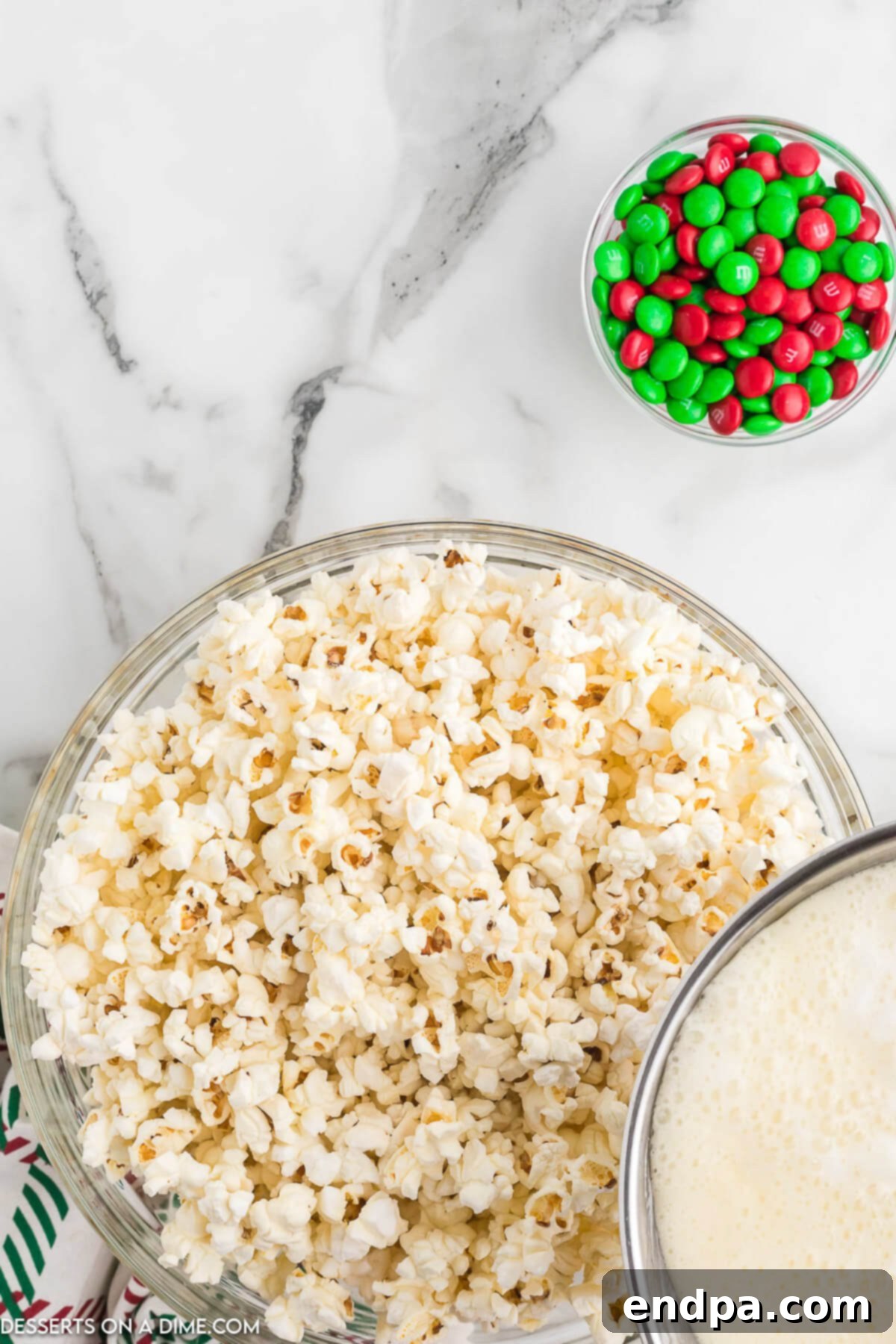 Holiday Popcorn Ball Delight 5 A close-up shot of warm popcorn in a very large mixing bowl, with the glossy, just-cooked syrup mixture being carefully drizzled over it from a saucepan, indicating the coating process has begun.