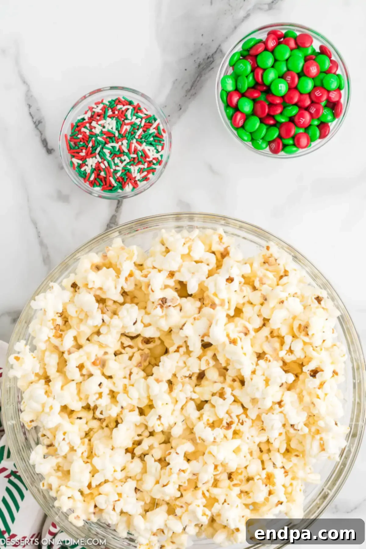 Holiday Popcorn Ball Delight 6 A large mixing bowl containing popcorn generously coated with the sweet syrup, along with festive red and green M&M's and Christmas sprinkles, all gently stirred and cooling slightly before being formed into balls.
