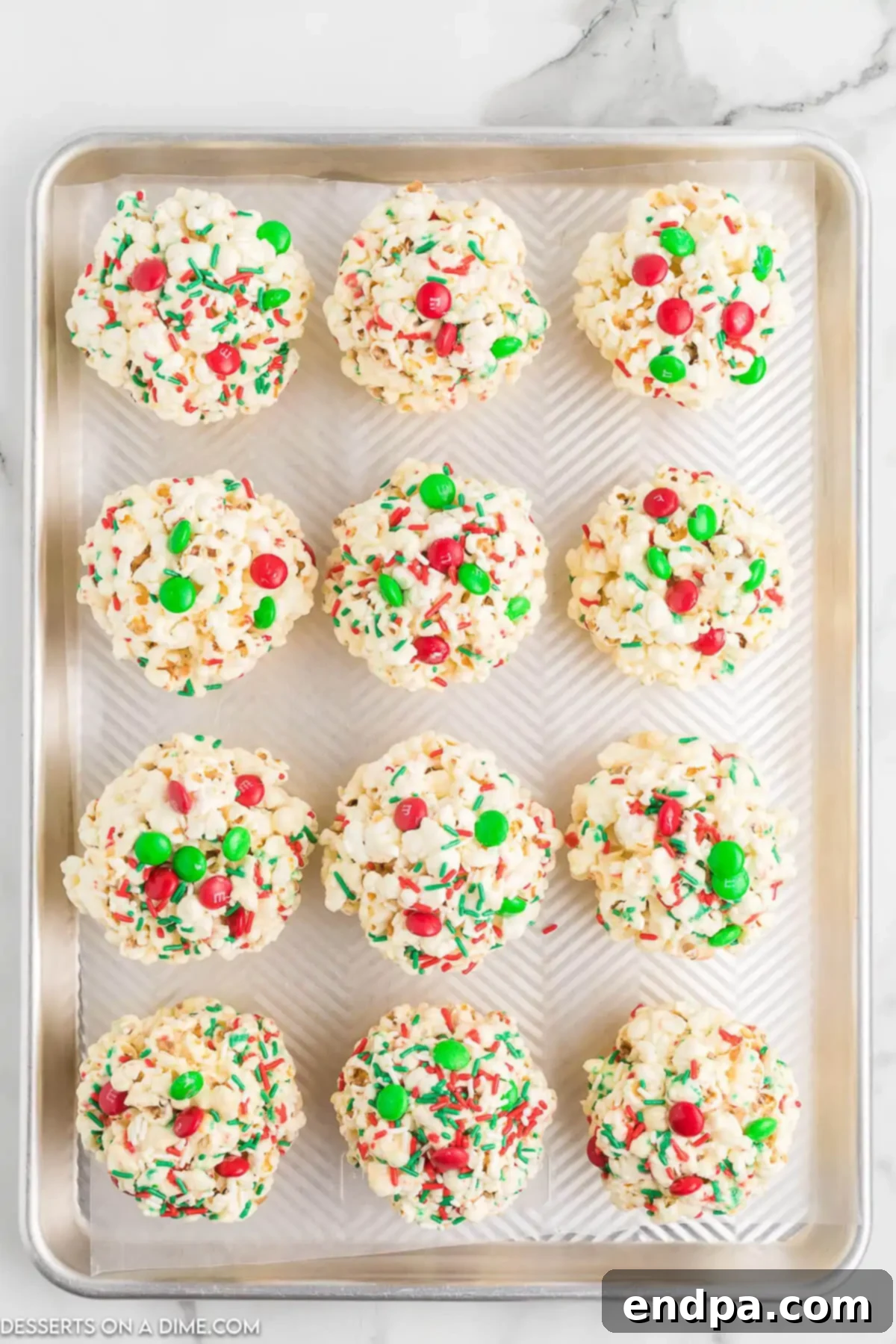 Holiday Popcorn Ball Delight 7 Several perfectly formed Christmas popcorn balls are neatly arranged on a baking sheet lined with parchment paper, allowing them to cool completely and set their shape.