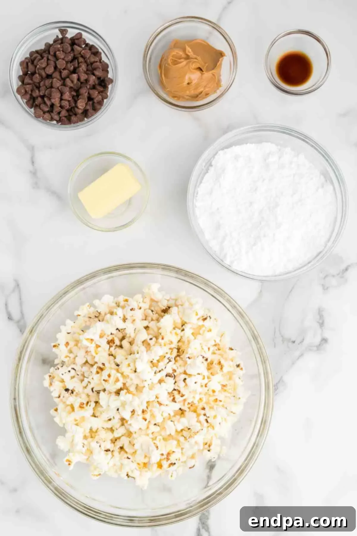 Muddy Buddy Popcorn Crunch 3 Ingredients for Puppy Chow Popcorn: popped popcorn, chocolate chips, peanut butter, vanilla extract, and powdered sugar, laid out on a surface.