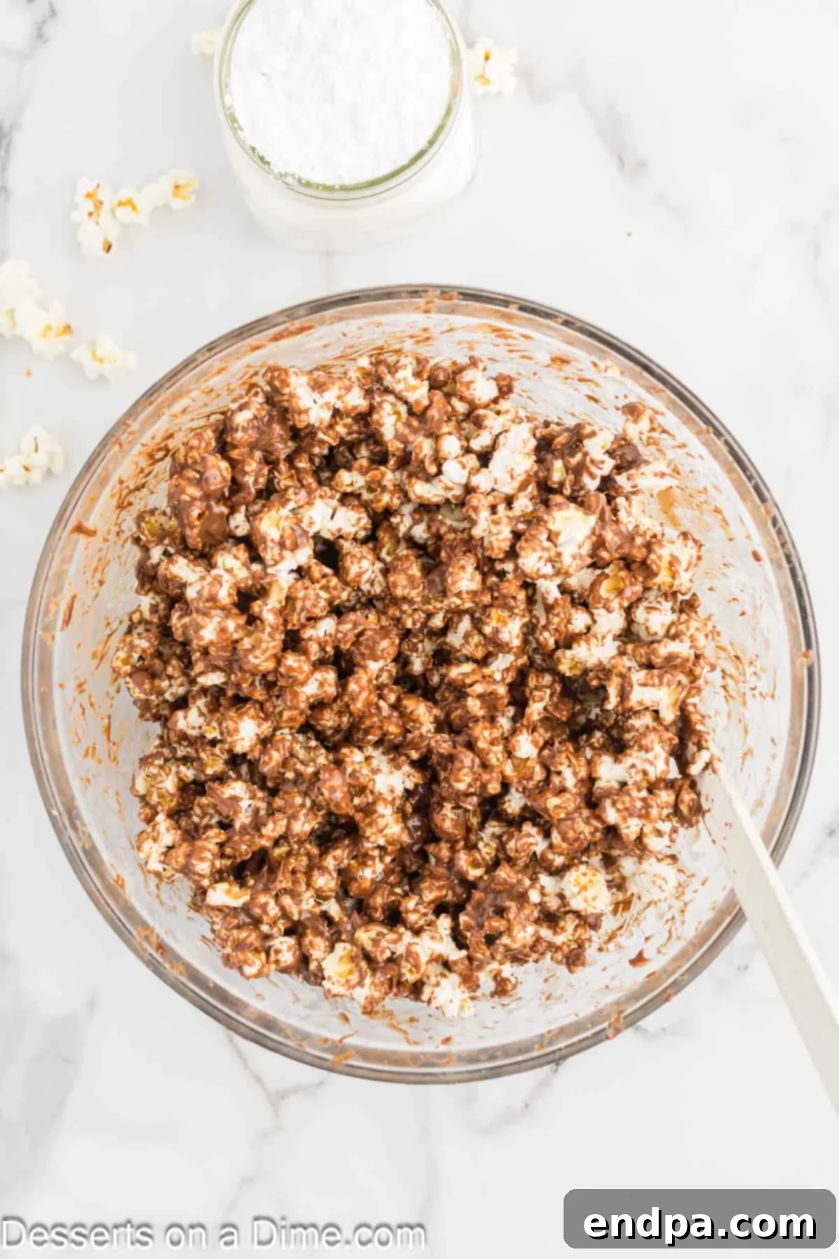 Muddy Buddy Popcorn Crunch 5 Warm chocolate coating being poured over popcorn in a large mixing bowl.