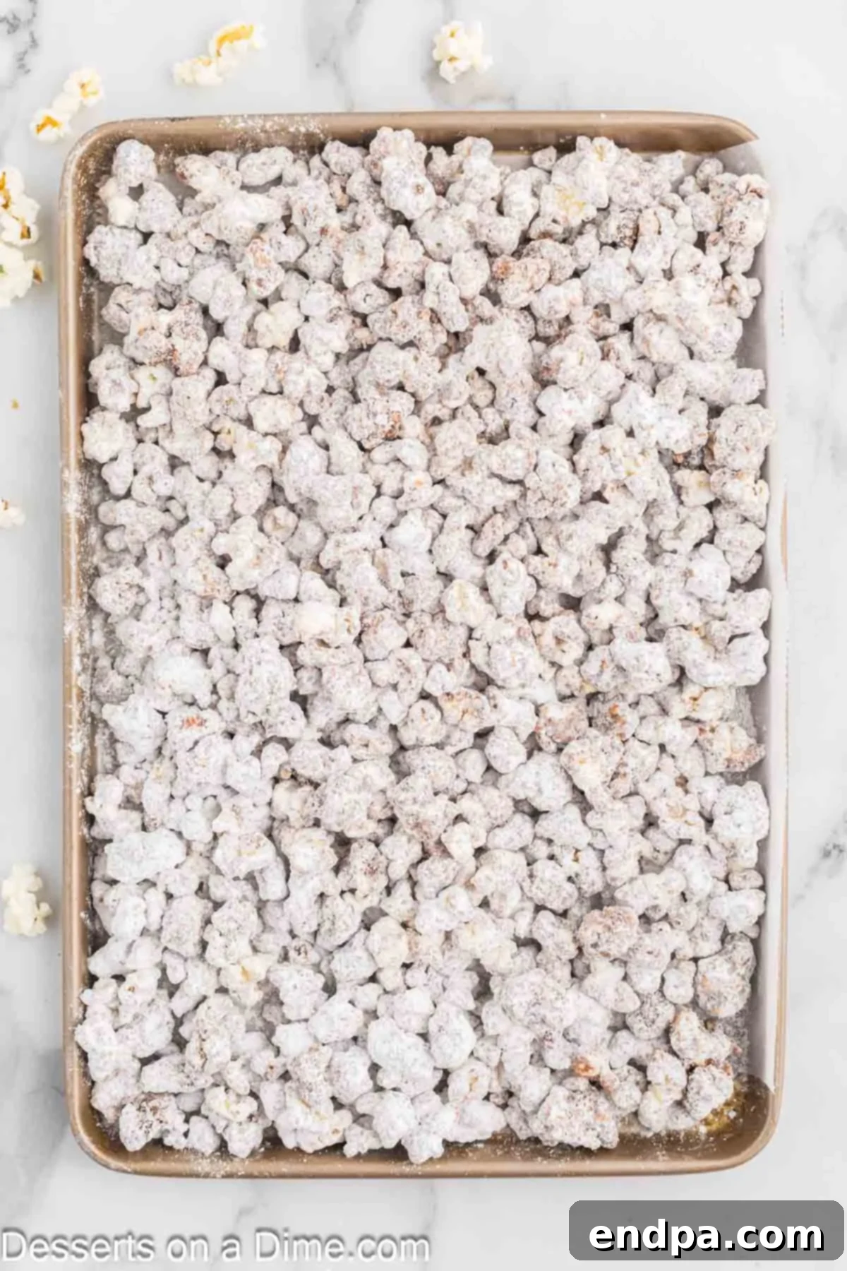 Muddy Buddy Popcorn Crunch 6 Powdered sugar-coated popcorn spread out on a baking sheet to cool.