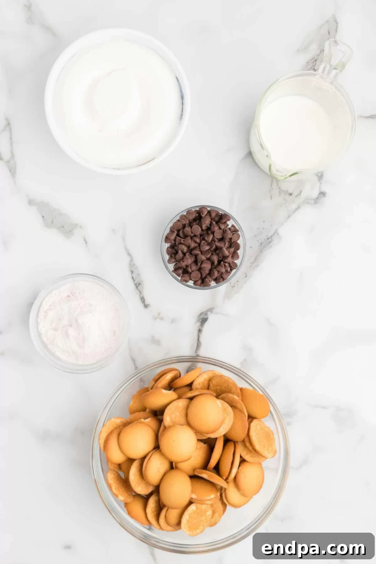 Eclair Cookie Fusion 3 A flat lay image displaying all the fresh ingredients required for making Eclair Cookies: vanilla wafers, a box of instant vanilla pudding mix, a glass of cold milk, a container of Cool Whip, and a bowl of semi-sweet chocolate chips.