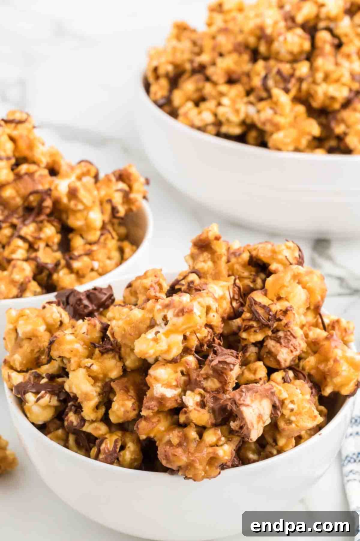 A bowl overflowing with freshly made Snickers popcorn, showcasing caramel-coated kernels, chopped Snickers pieces, and a generous chocolate drizzle.