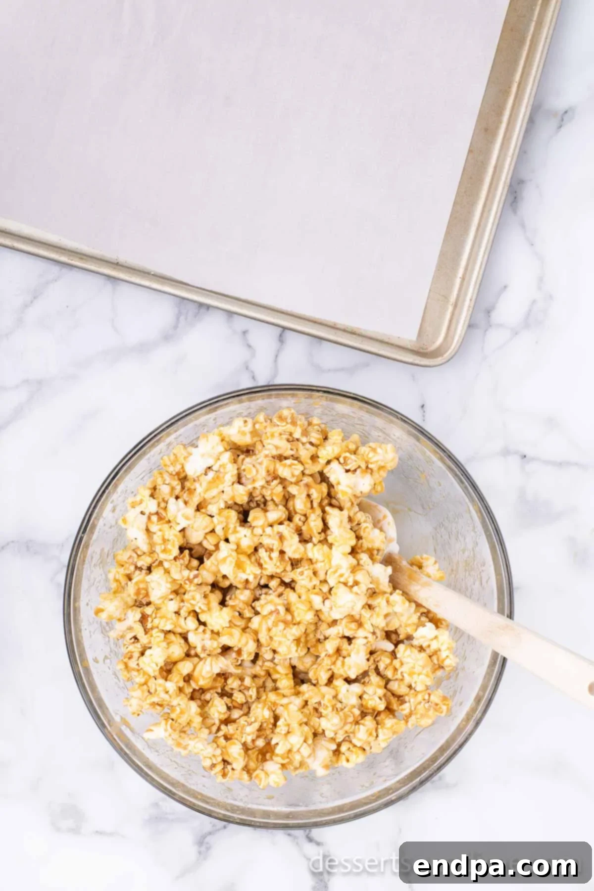 Freshly popped popcorn being coated with warm, golden caramel sauce in a large bowl.