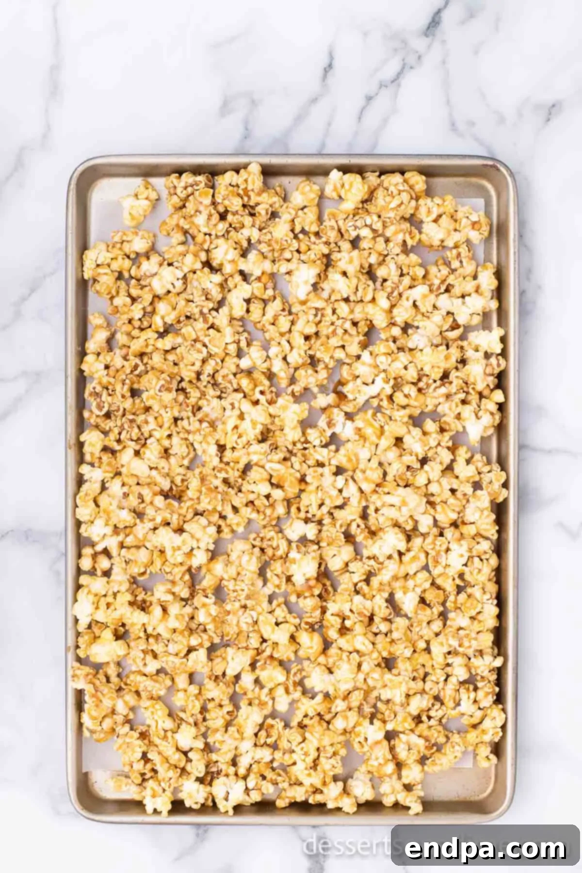 Caramel-coated popcorn spread out in a thin layer on a baking sheet, ready for the oven.