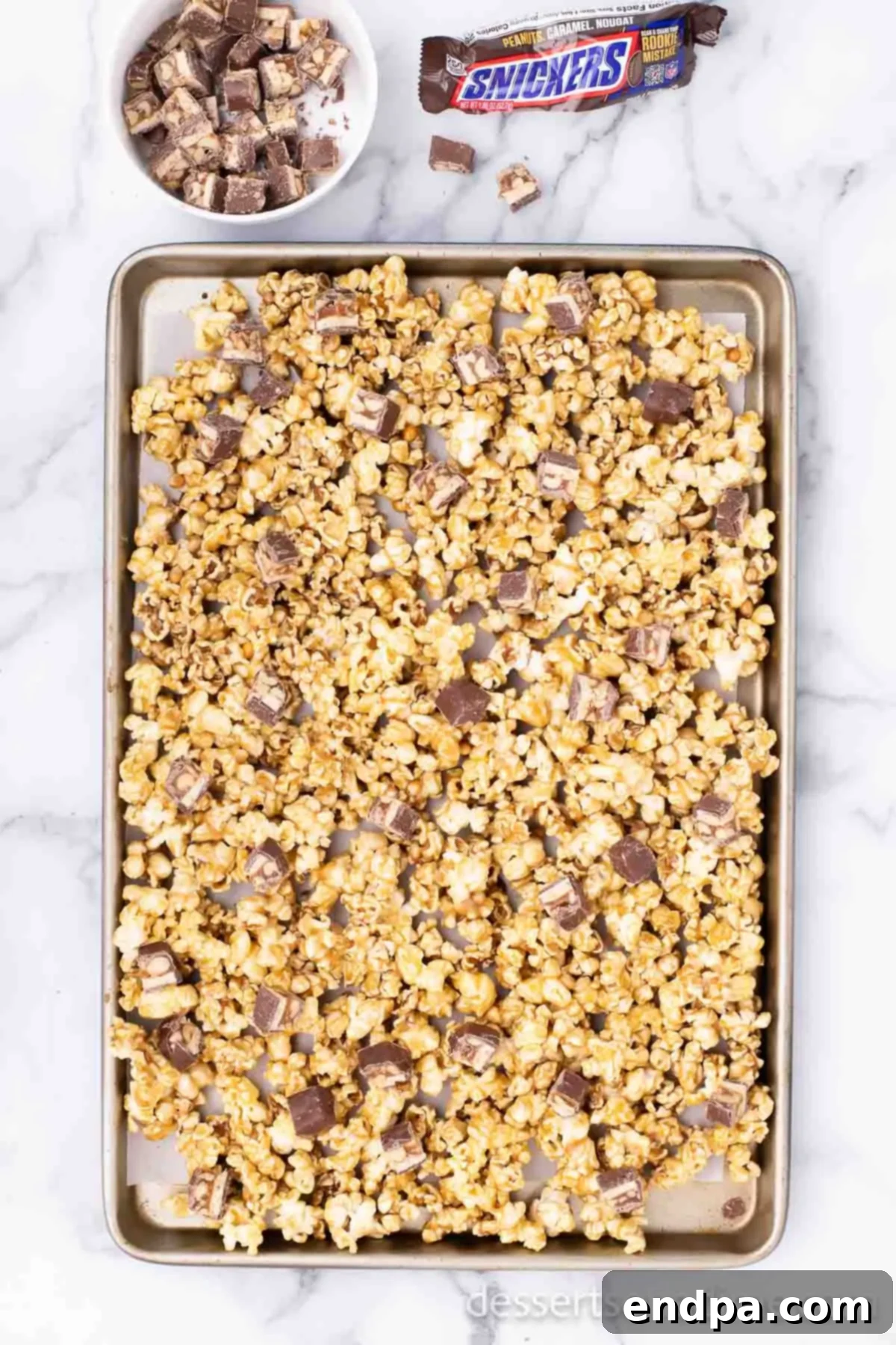 Chopped Snickers candy bar pieces being mixed into the warm, baked caramel popcorn.