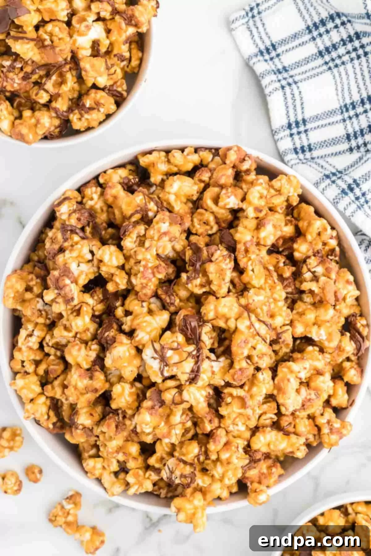 A large bowl of finished Snickers popcorn, gleaming with caramel, chocolate, and candy bar chunks, ready to be enjoyed.