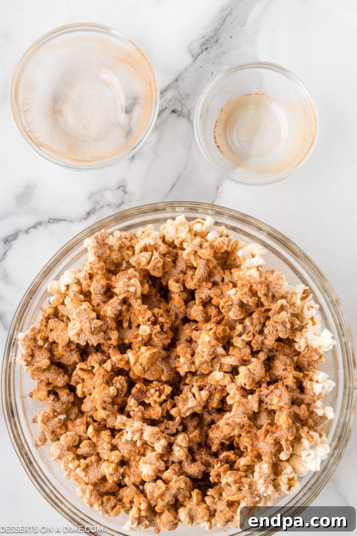 A large bowl of popcorn being tossed with the cinnamon and sugar mixture, showing an even coating.