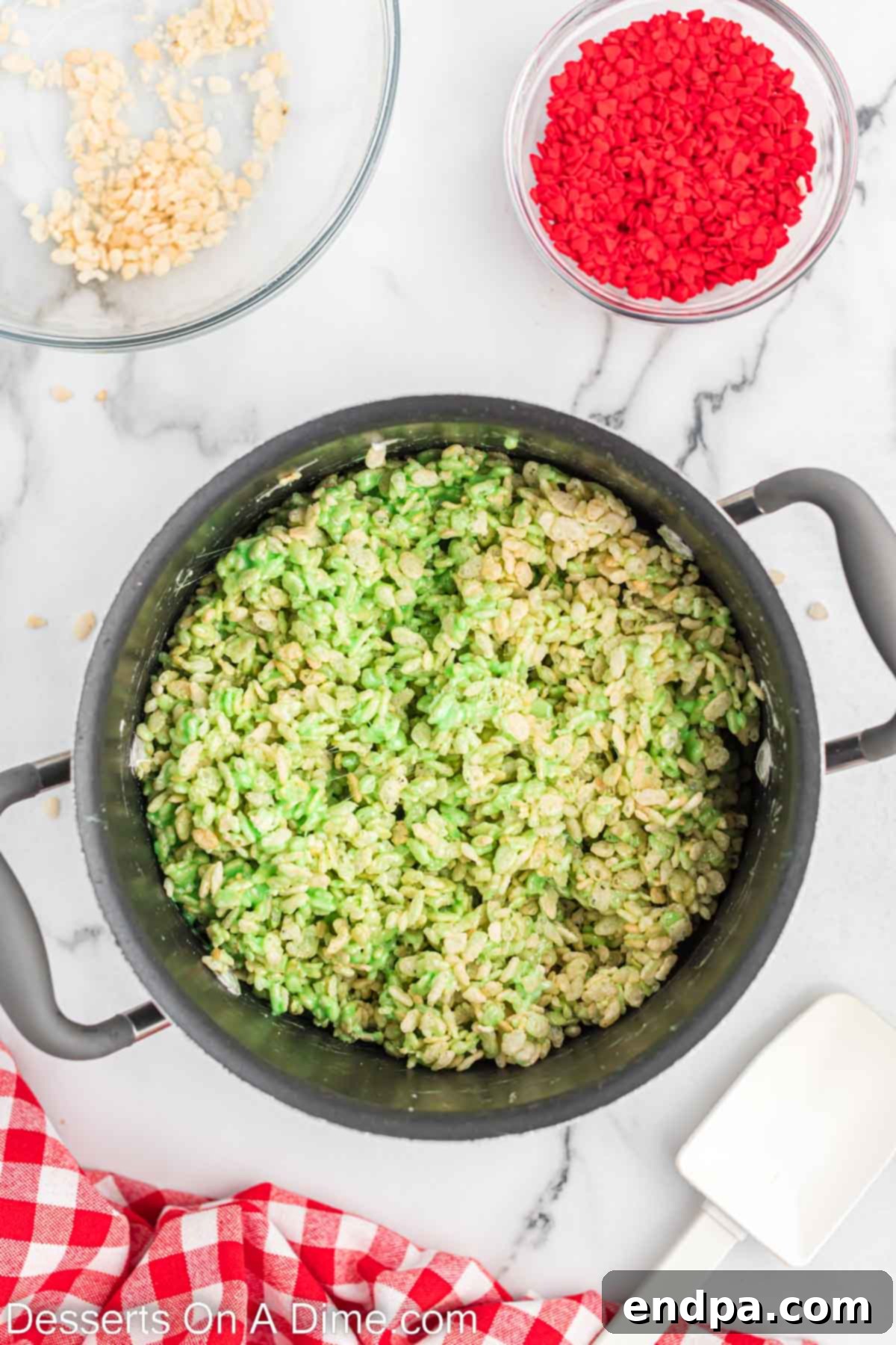 Rice Krispie cereal being folded into the green marshmallow mixture in a large saucepan.