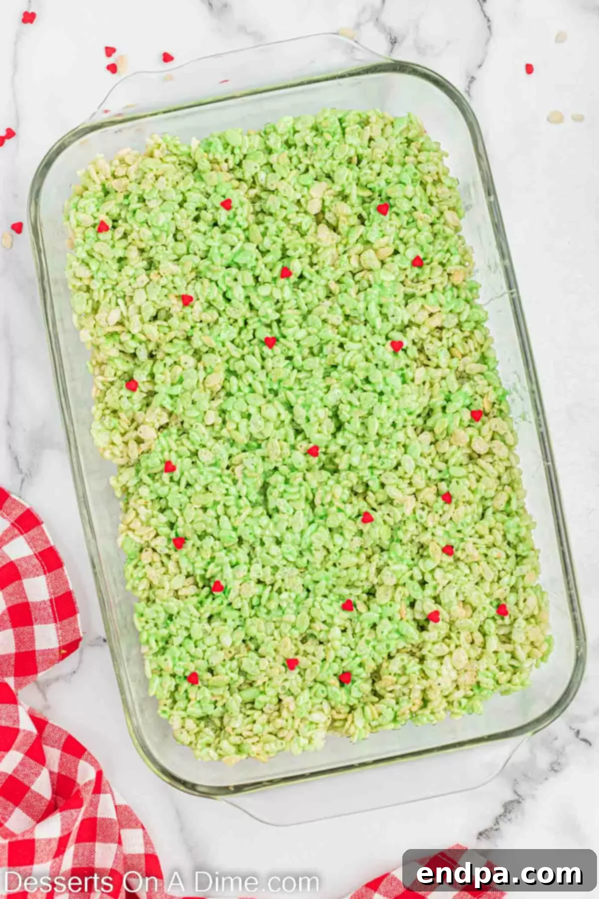 Red heart sprinkles scattered generously over the top of the green Rice Krispie treats in the pan.