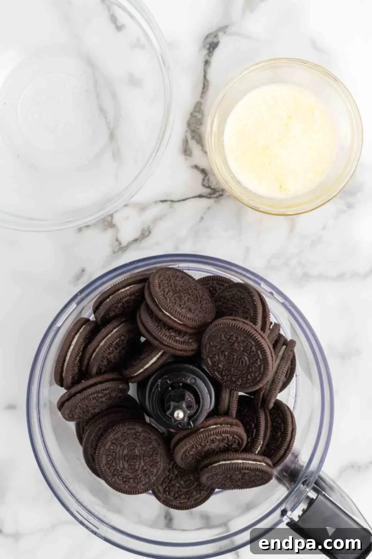 Crushing Oreo cookies in a food processor to prepare the pie crust. The processor bowl is filled with dark cookie crumbs, ready for the next step.