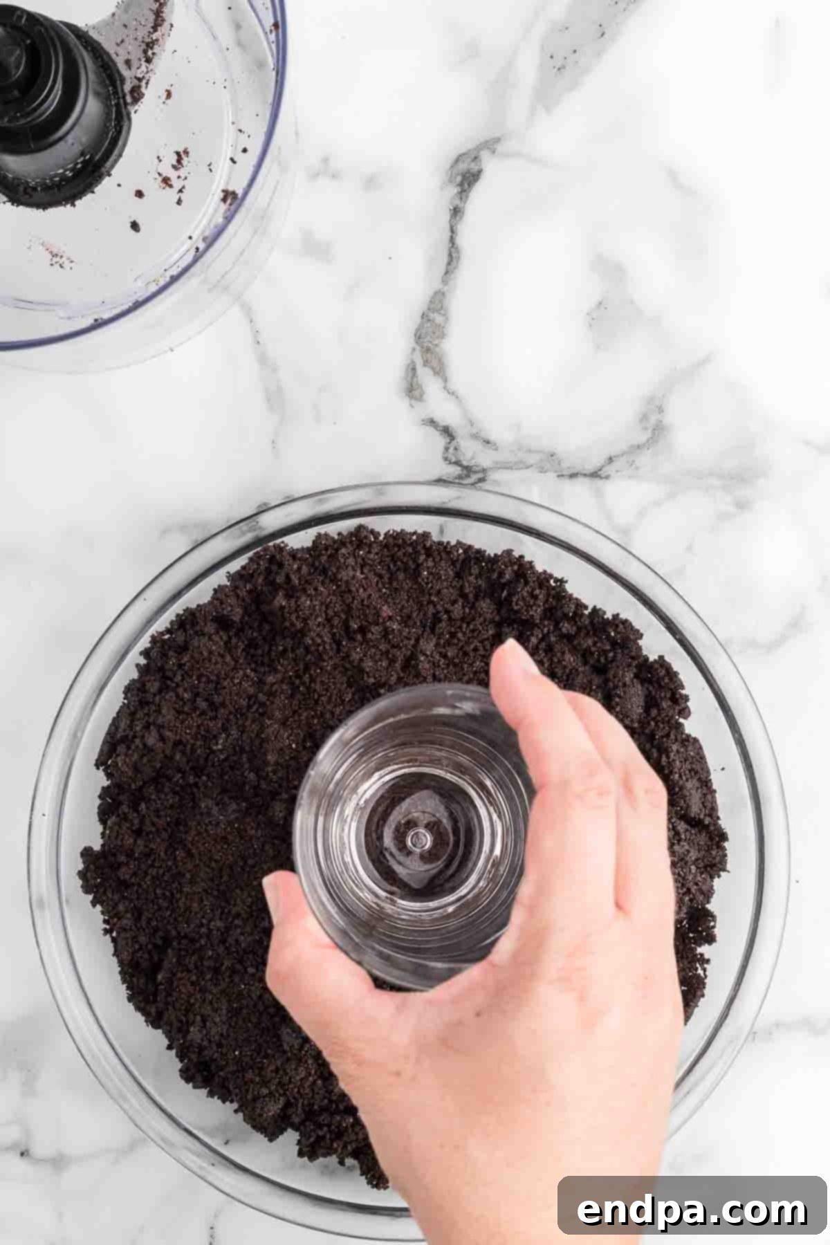 Mixing crushed Oreo cookies with melted butter in a bowl. A spatula is being used to combine the dark crumbs with the golden liquid, creating a uniform mixture for the pie crust.