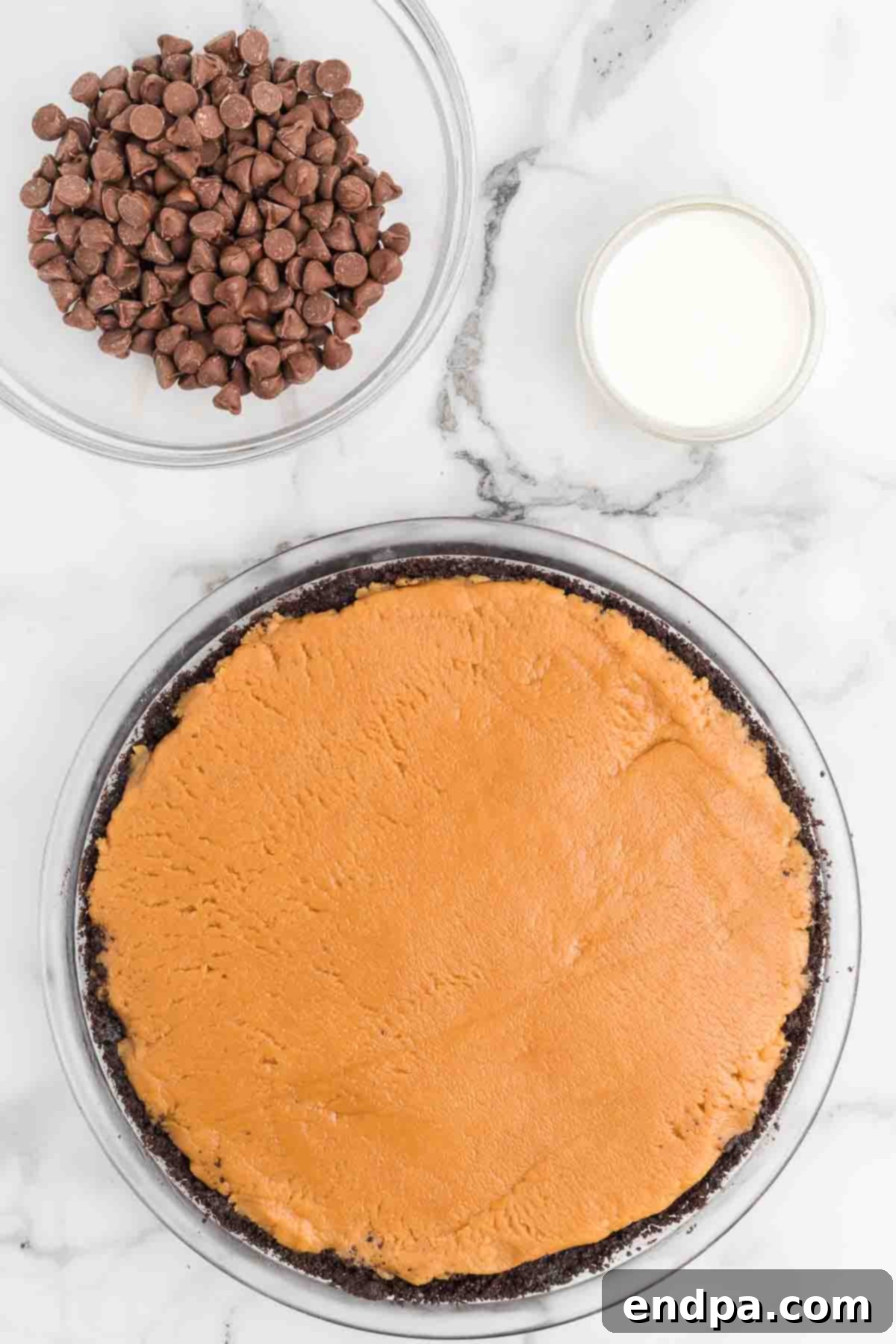 Spreading the light-colored peanut butter mixture evenly into the dark, prepared Oreo pie crust using a spatula, creating a smooth, flat layer.
