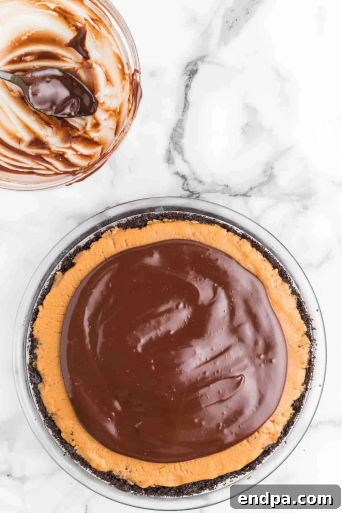 Carefully spooning and spreading the melted chocolate ganache onto the peanut butter filling of the pie, leaving a visible border of the peanut butter layer for the traditional buckeye look.