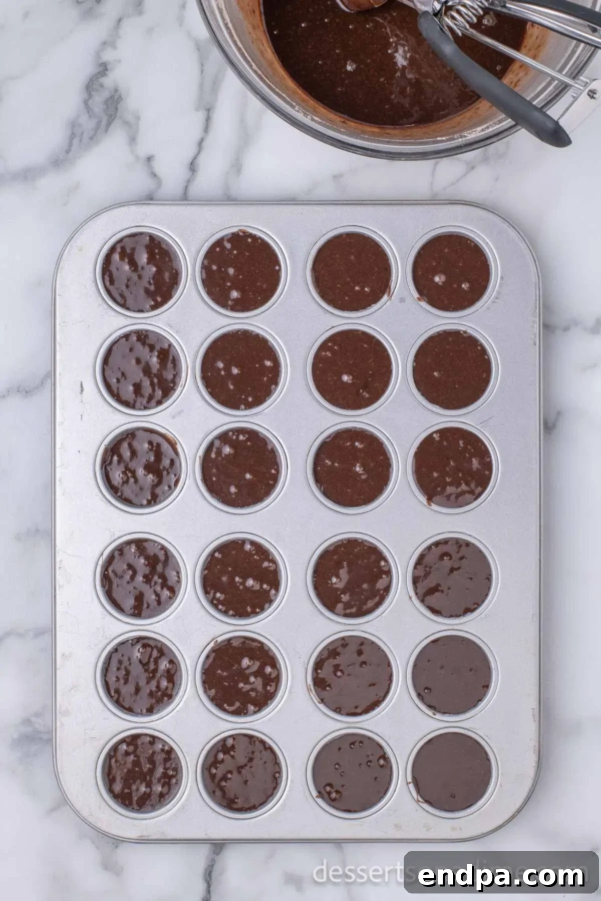 Ho-Ho-Ho Brownie Hats 3 Brownie batter being carefully spooned into individual cups of a greased mini muffin pan, preparing for baking.