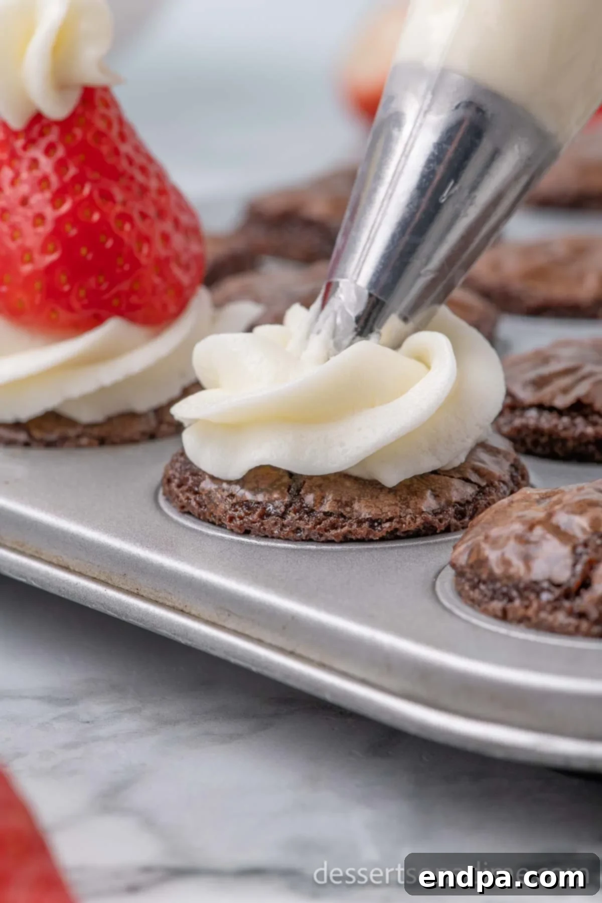 Ho-Ho-Ho Brownie Hats 6 A mini brownie bite being piped with a generous swirl of white frosting, forming the base of the Santa hat.