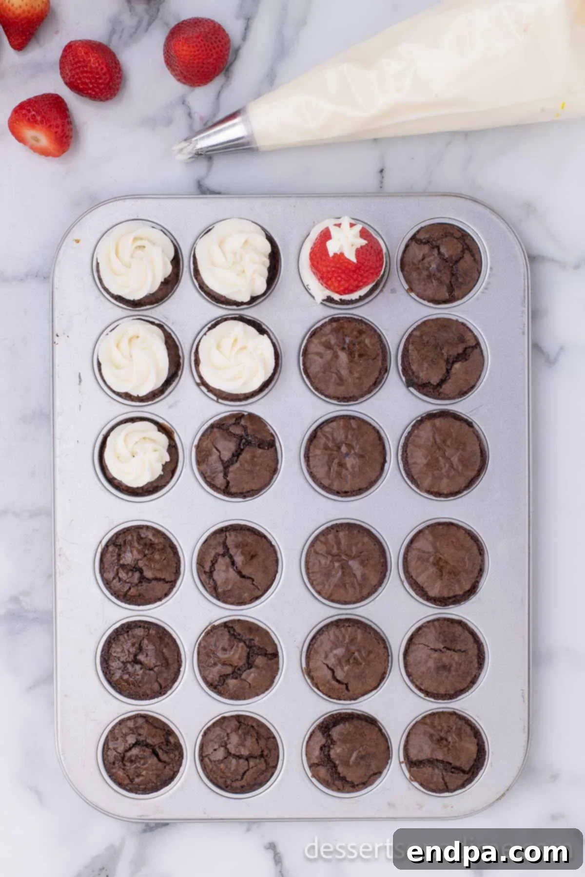 Ho-Ho-Ho Brownie Hats 7 A fresh, hulled strawberry carefully placed on the white frosting swirl of a brownie bite, with a final small dollop of frosting added to the strawberry's tip to complete the Santa hat look.