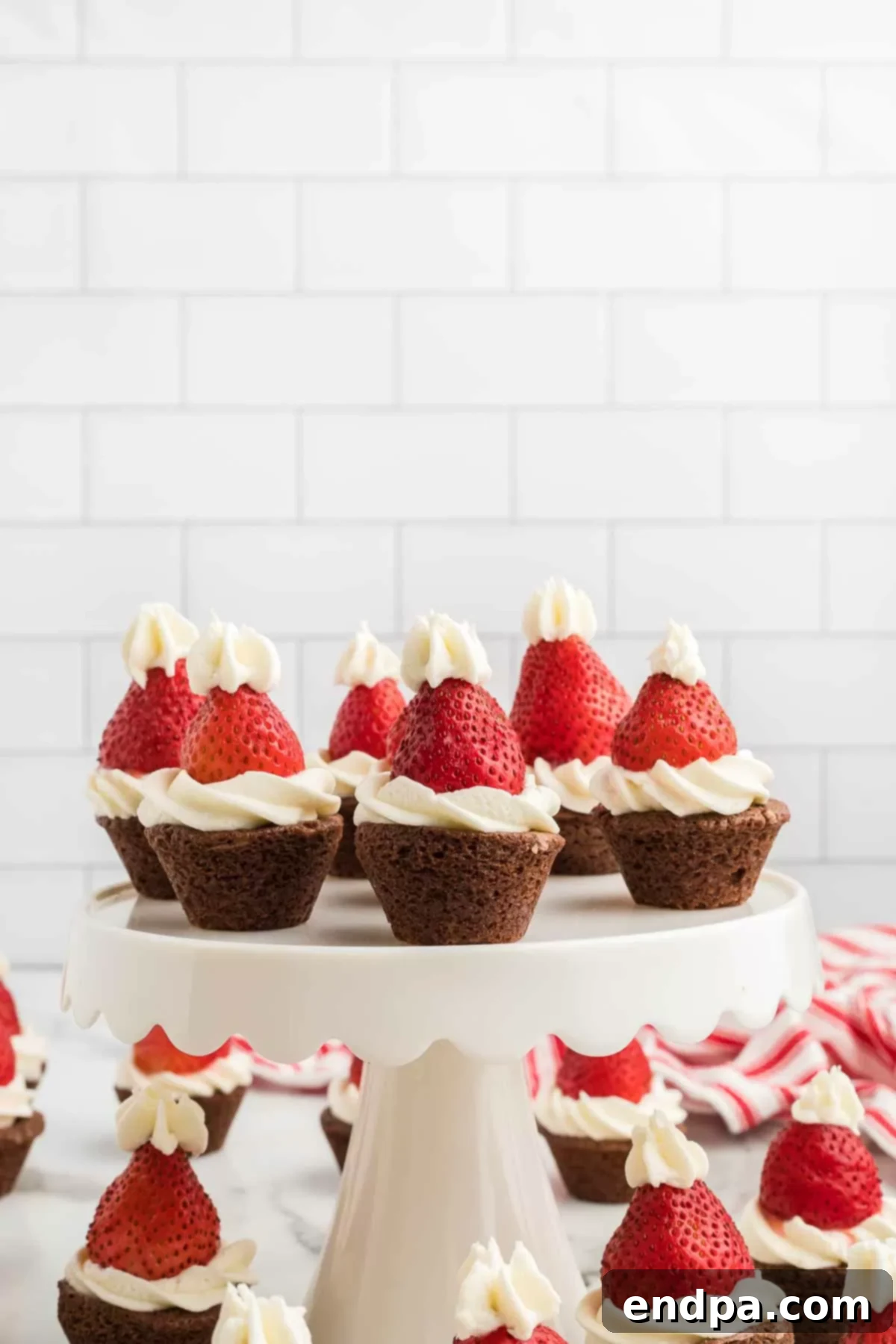 Ho-Ho-Ho Brownie Hats 9 An array of delicious Santa hat brownie bites artfully arranged on a two-tiered pedestal, making a perfect centerpiece for a festive occasion.